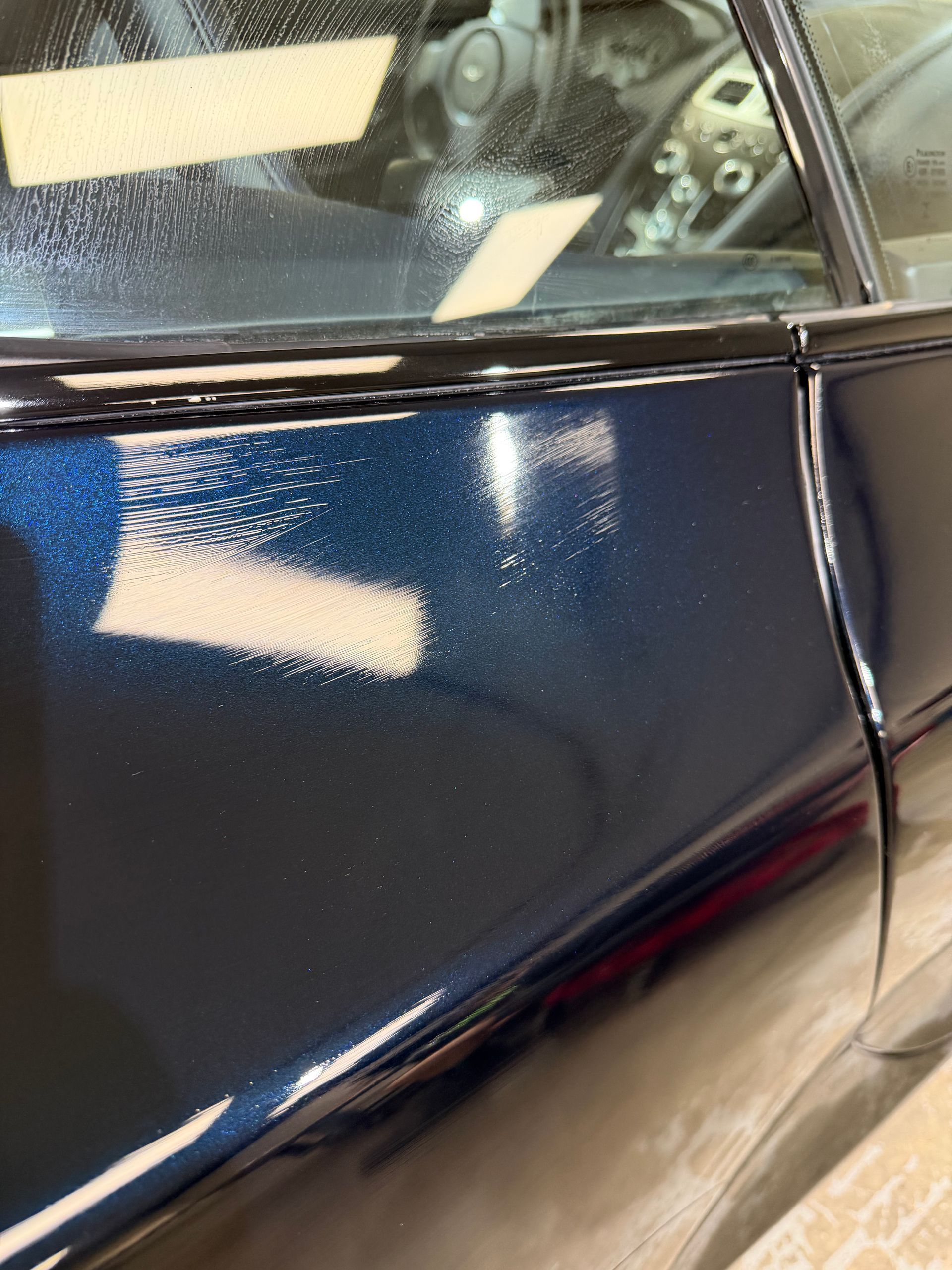 Close-up of a dark blue car door with a dent and scuff marks near the window trim