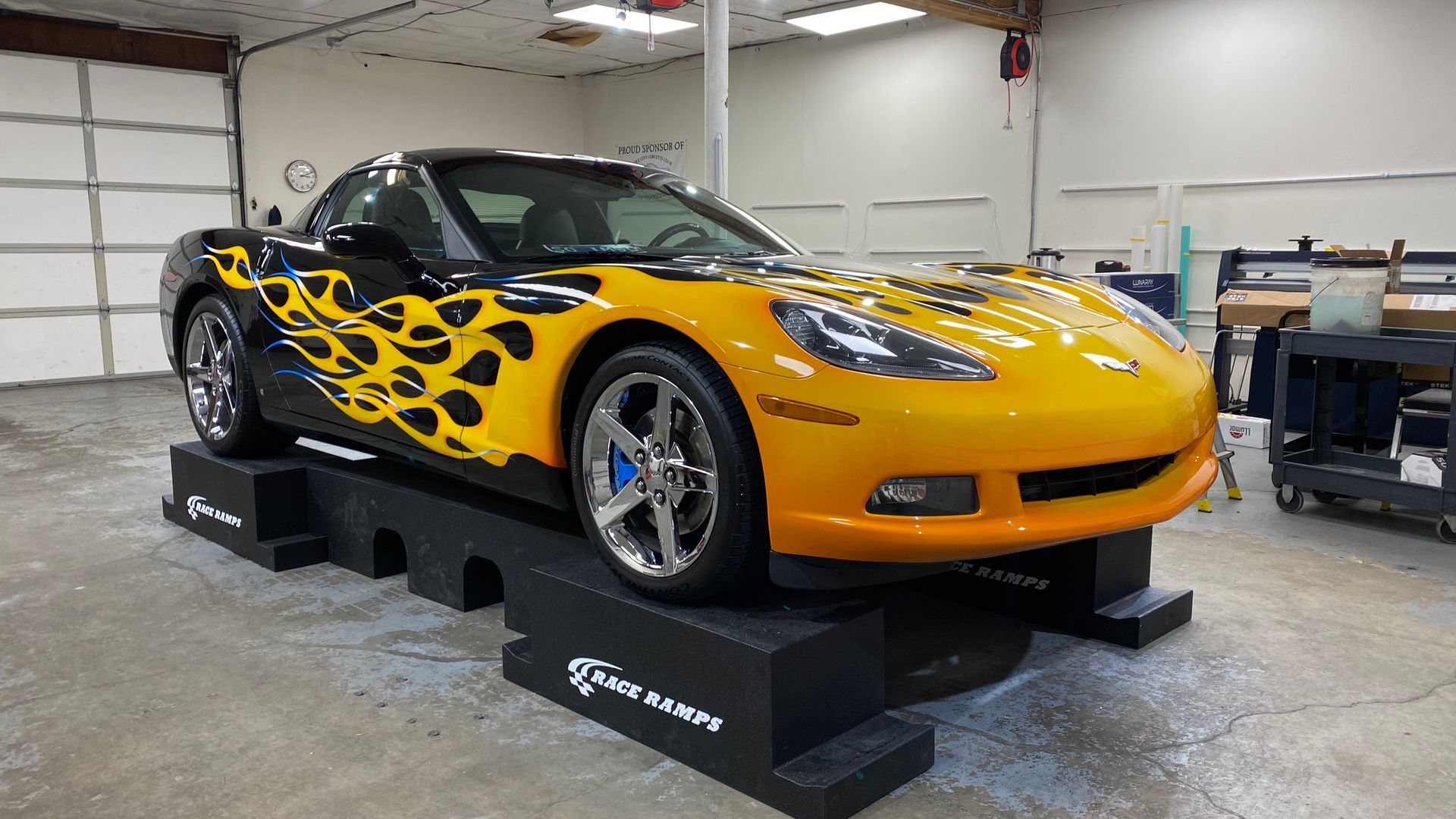 Yellow sports car with black flame decals displayed indoors on a lift platform