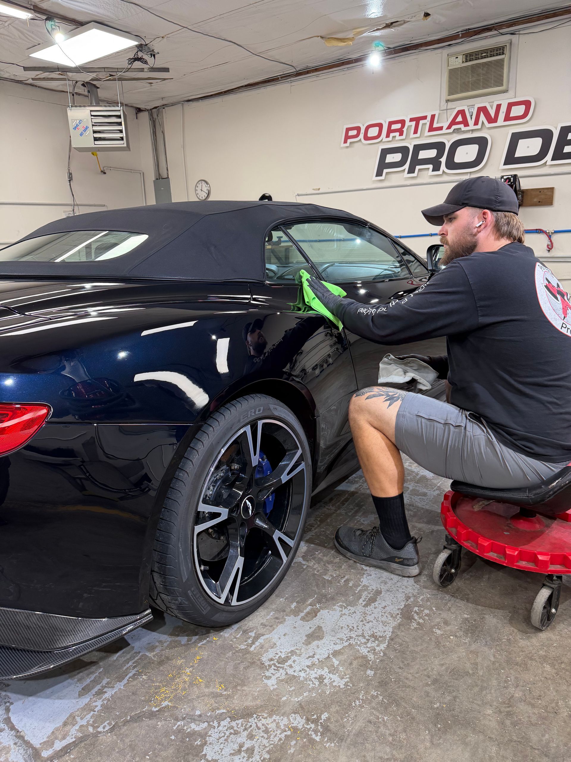 Detailer polishing a black car in a Portland Pro shop using a green cloth and buffer.
