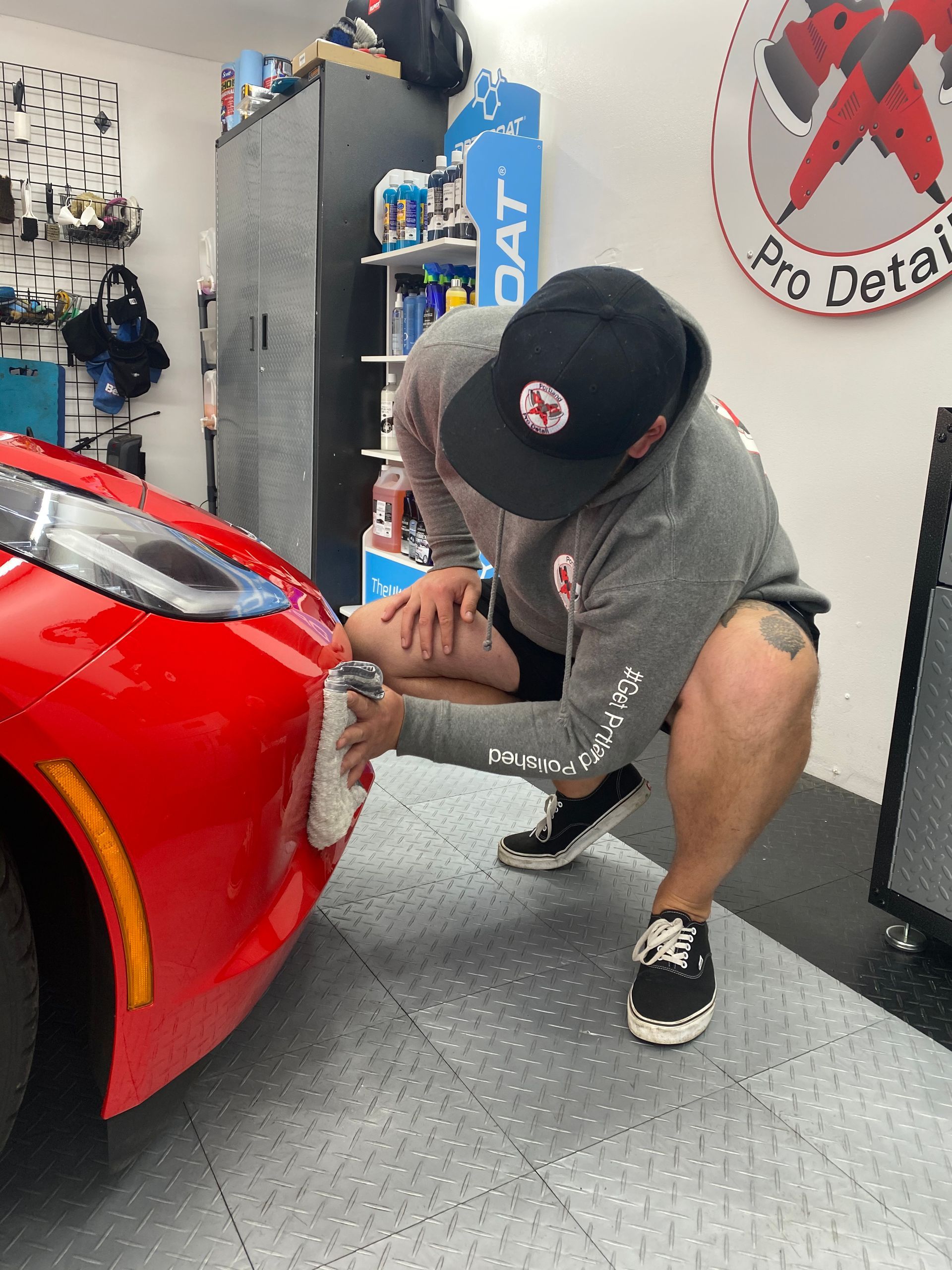 Person kneeling beside a red car, applying detailing work in a garage
