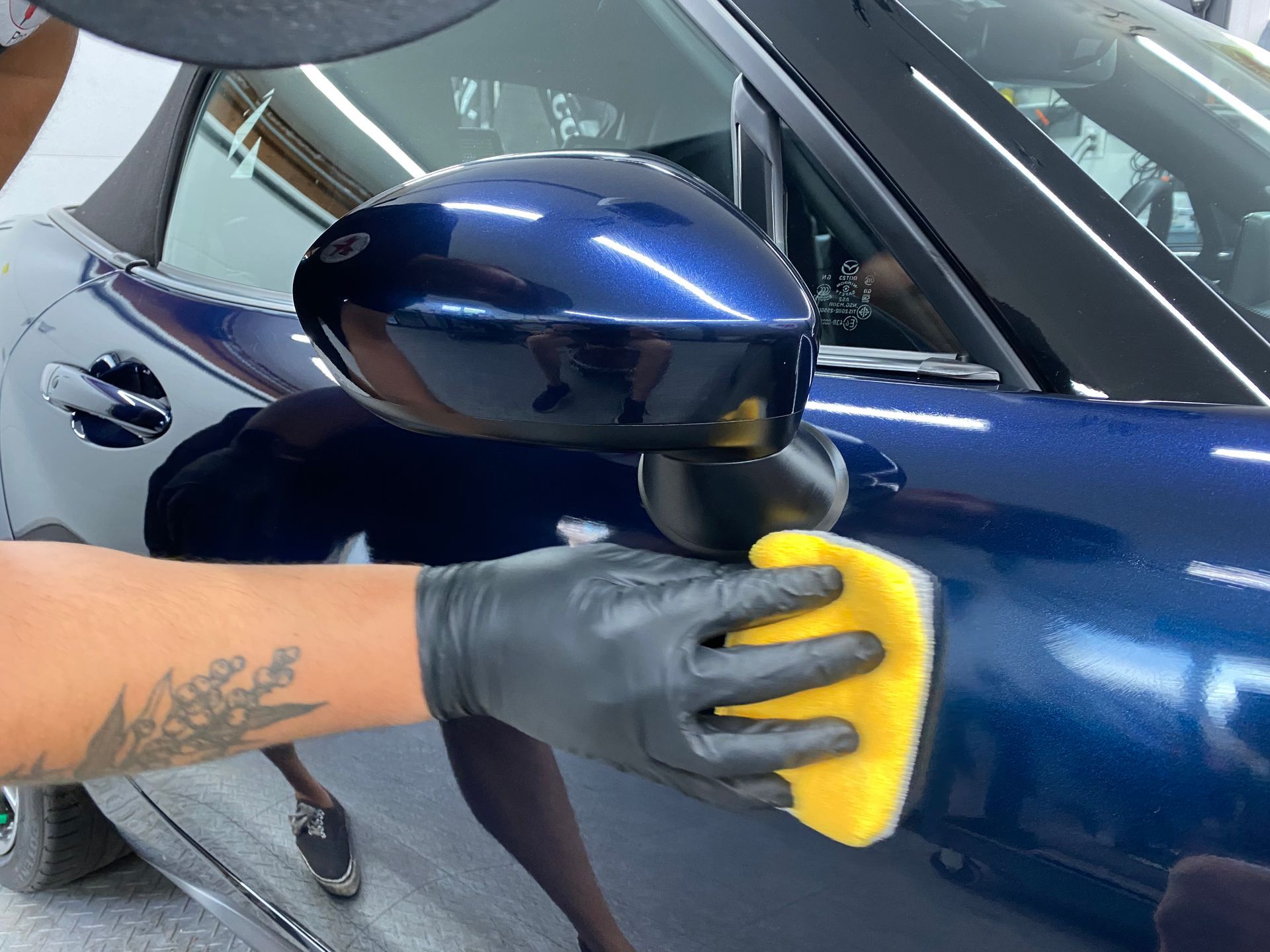 Gloved hand polishing a blue car’s side mirror and door with a yellow sponge