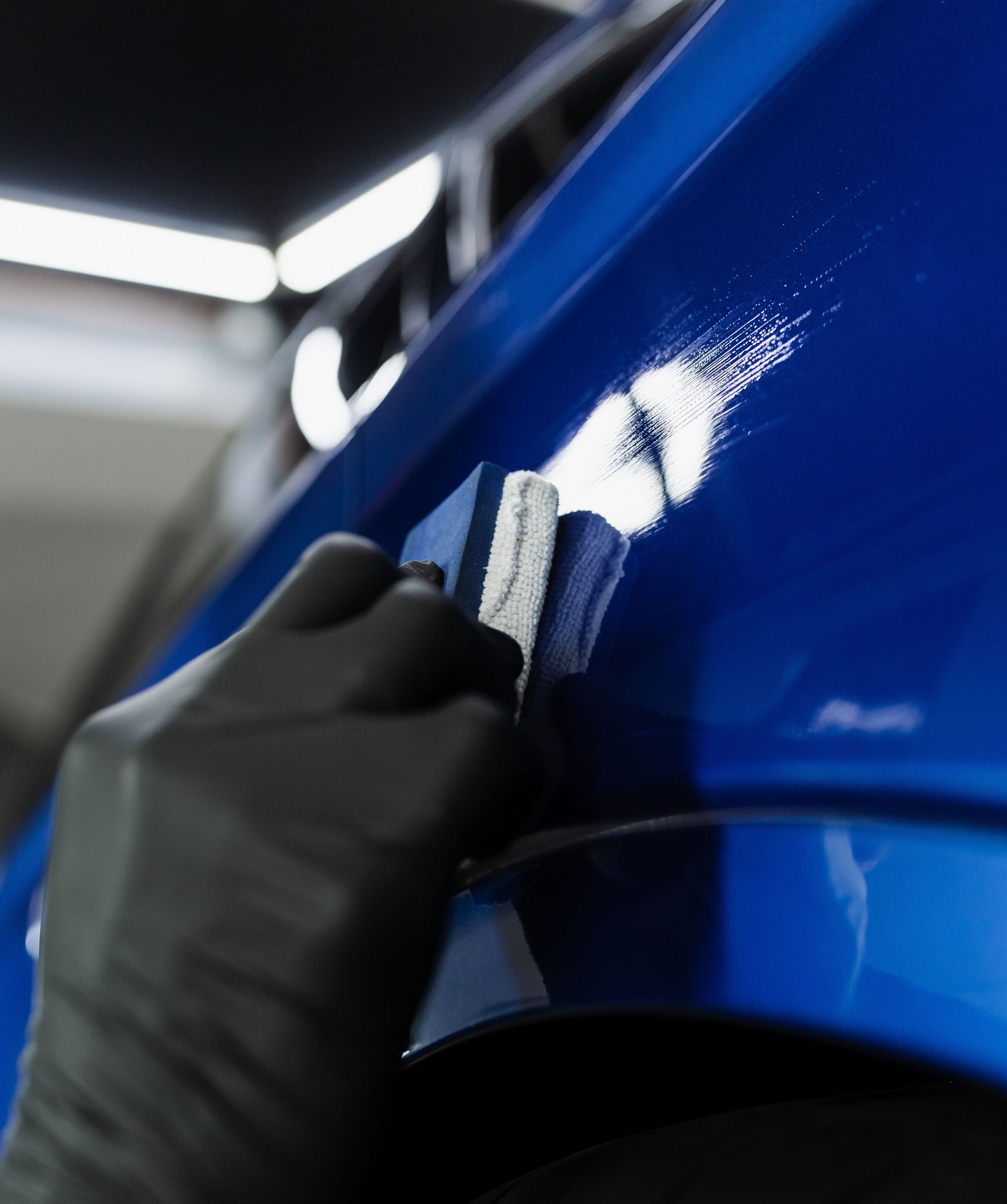 Gloved hand polishing a glossy blue car panel with a cloth