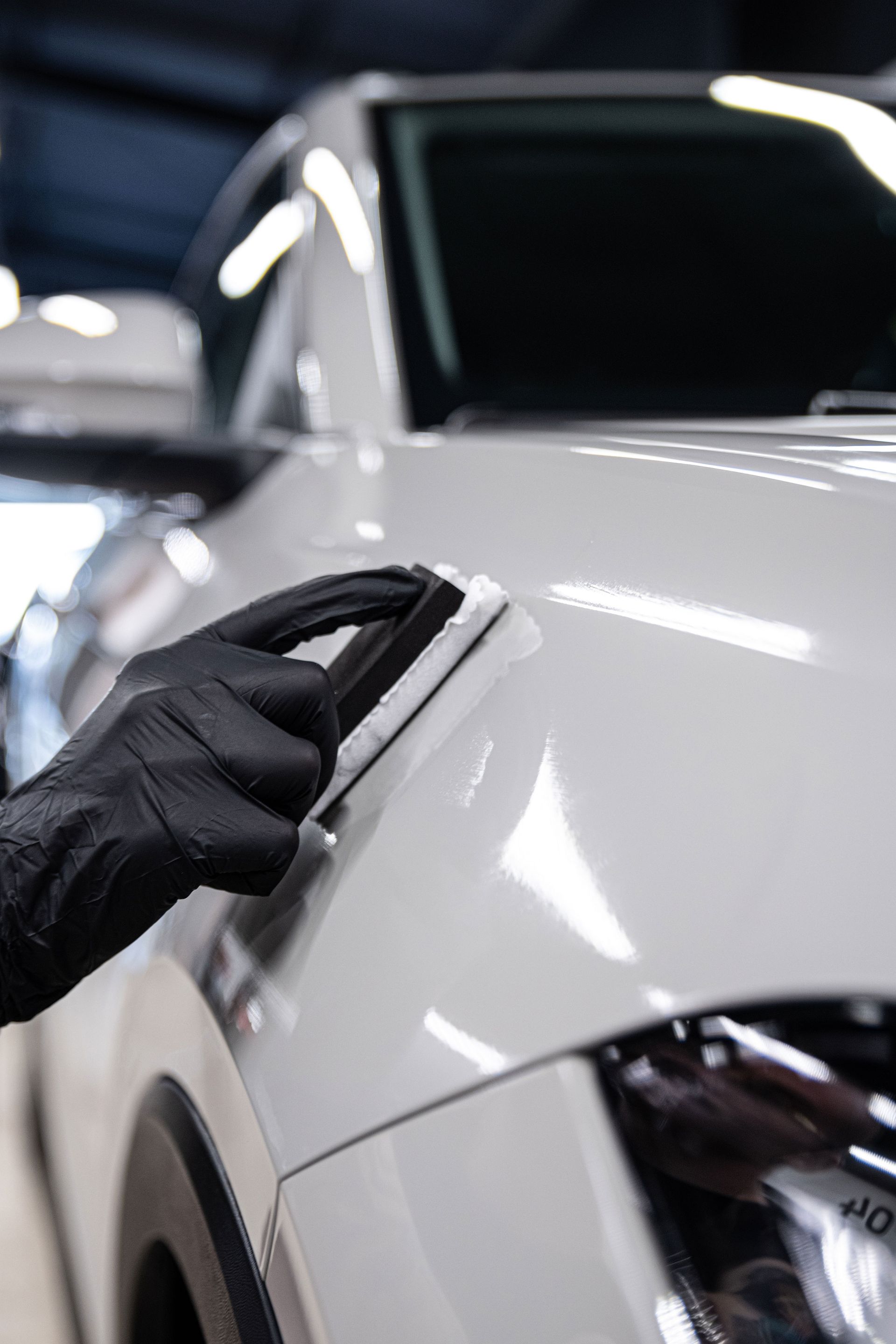 Black-gloved hand polishing a white car hood in a garage