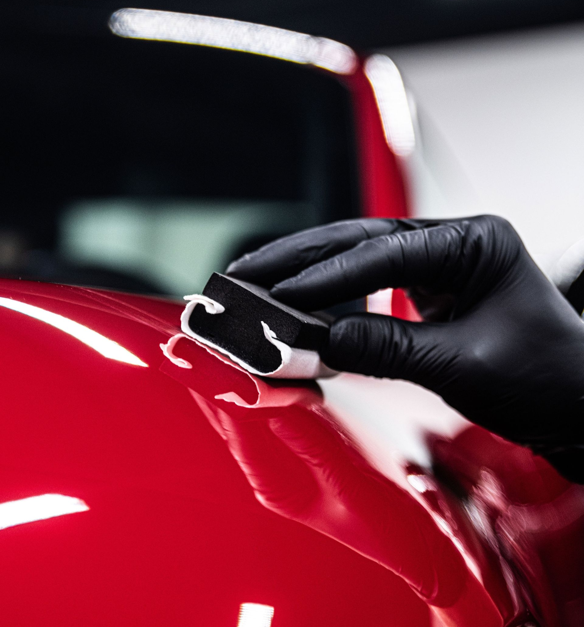 Gloved hand polishing a glossy red car panel with a cloth under bright lights