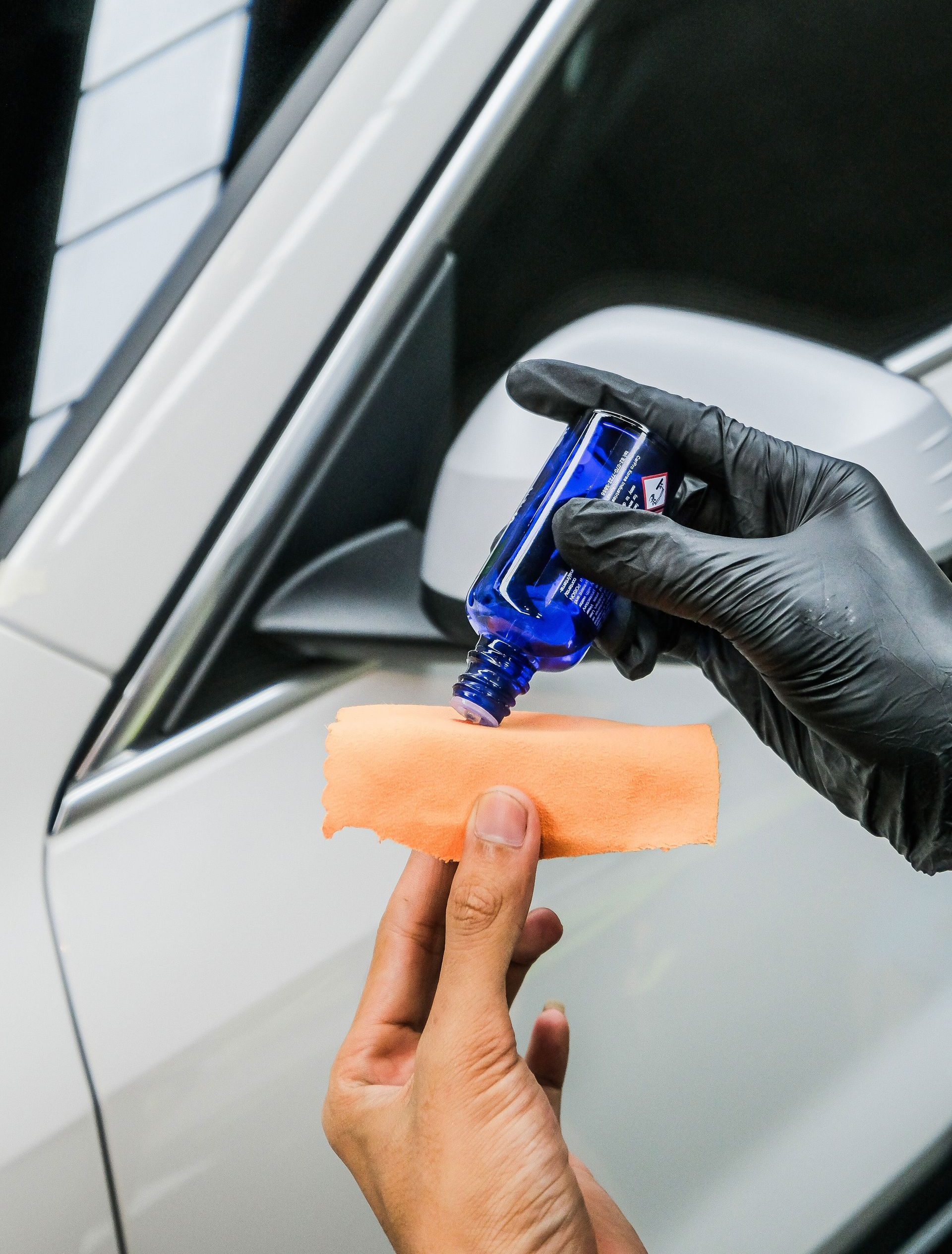 Gloved hands apply blue film to a car window with a squeegee tool