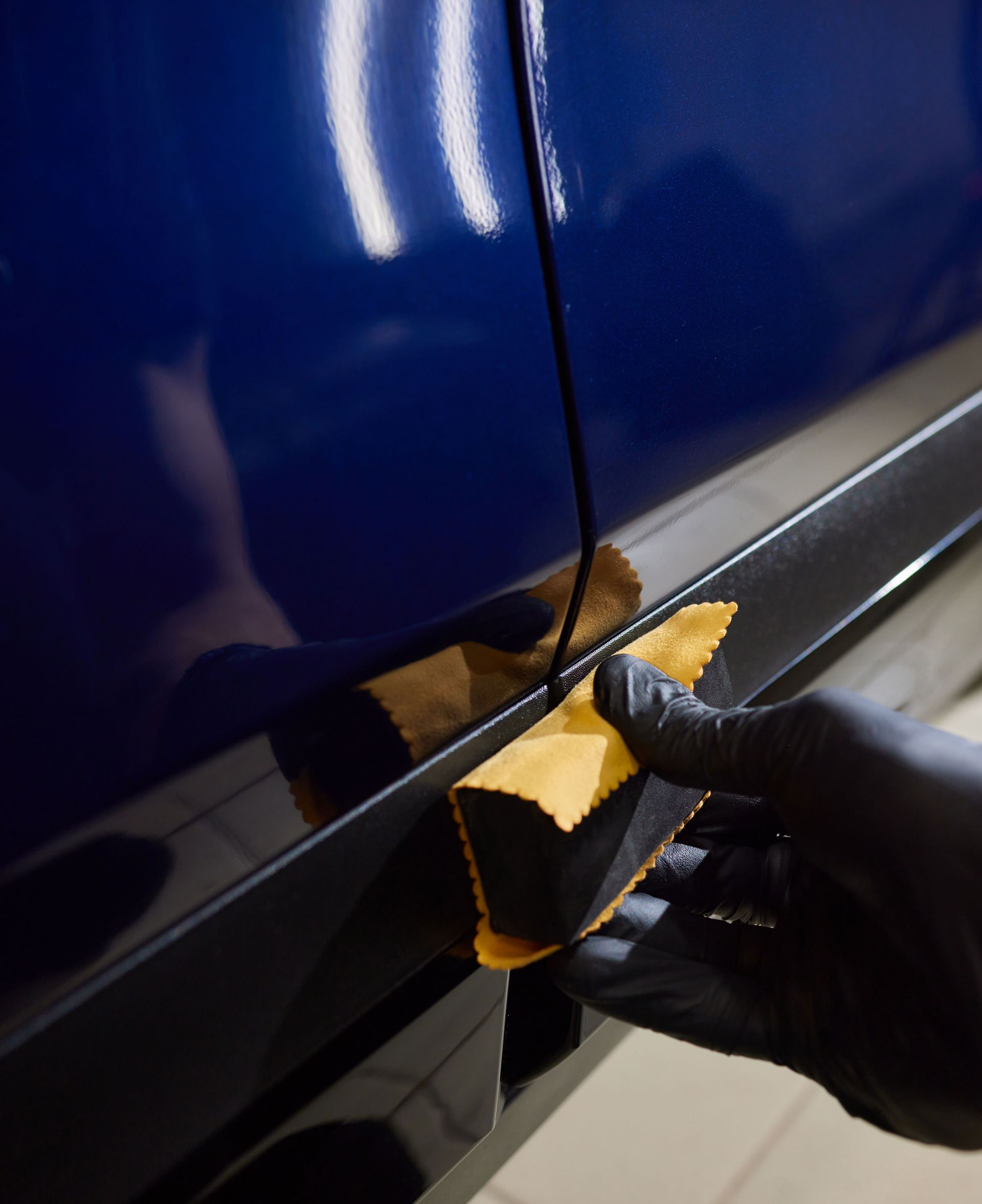 Gloved hand applying gold vinyl wrap to a blue car door seam