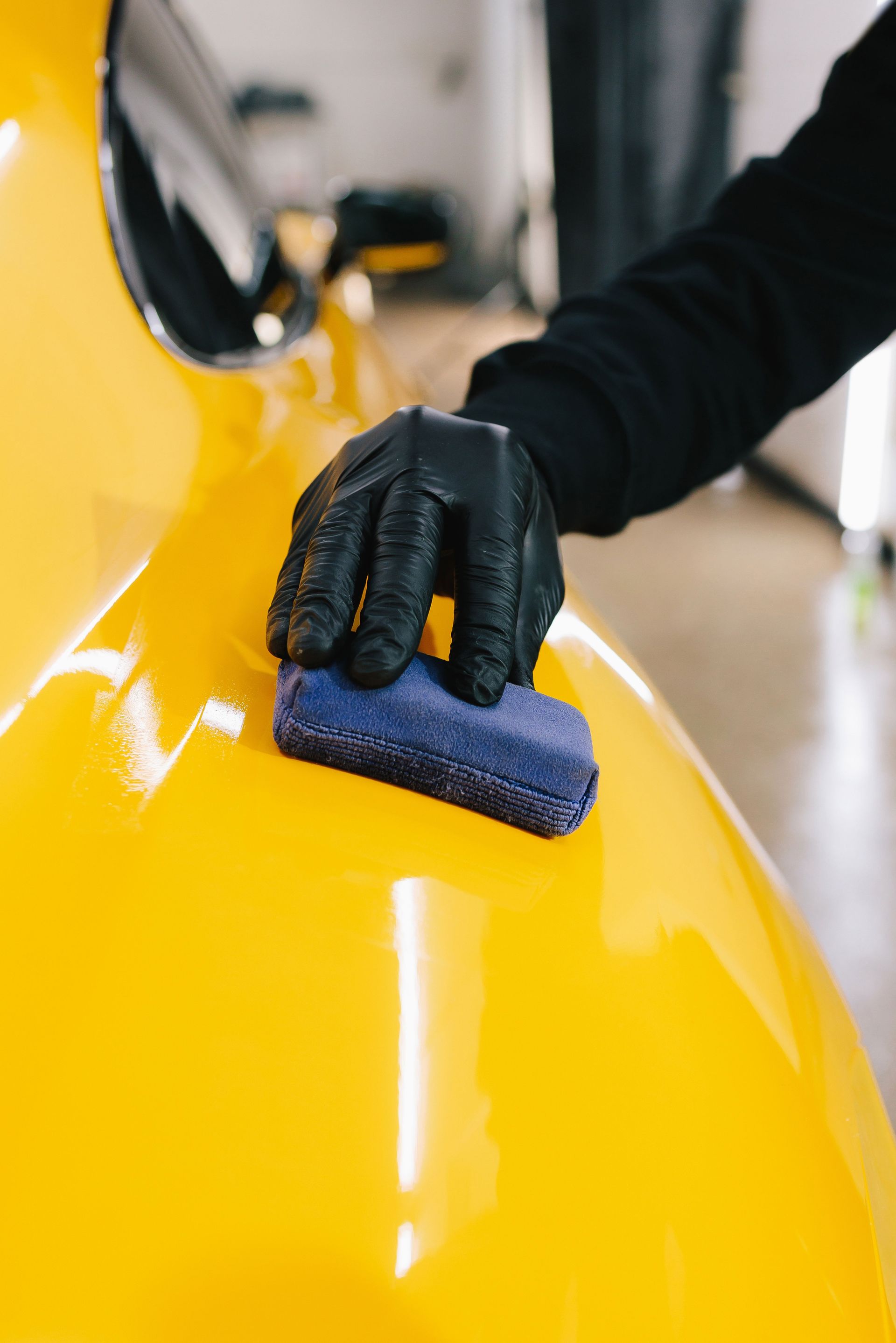 Gloved hand polishing a bright yellow car with a blue cloth