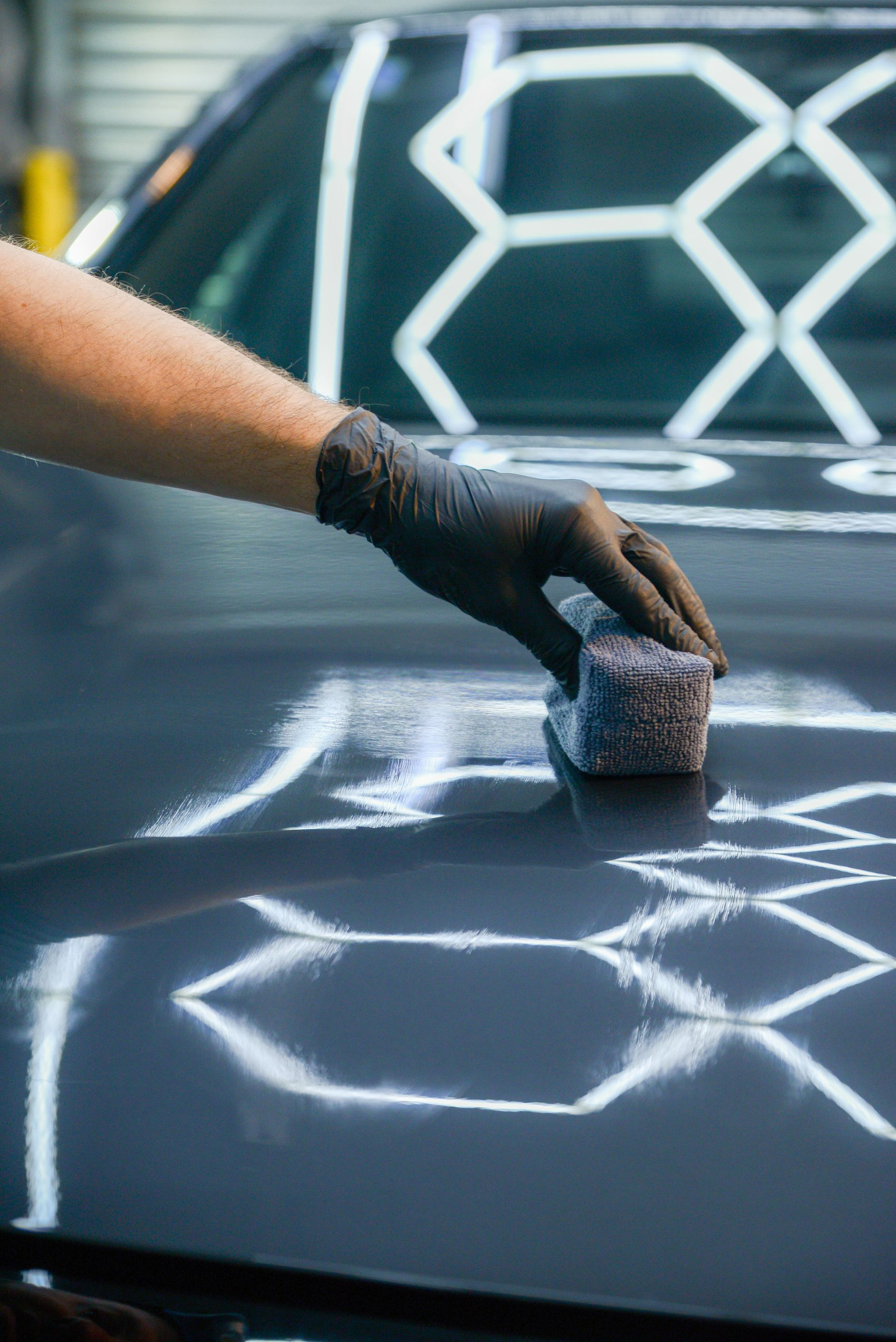 Gloved hand painting white geometric lines on a dark car hood with a sponge applicator