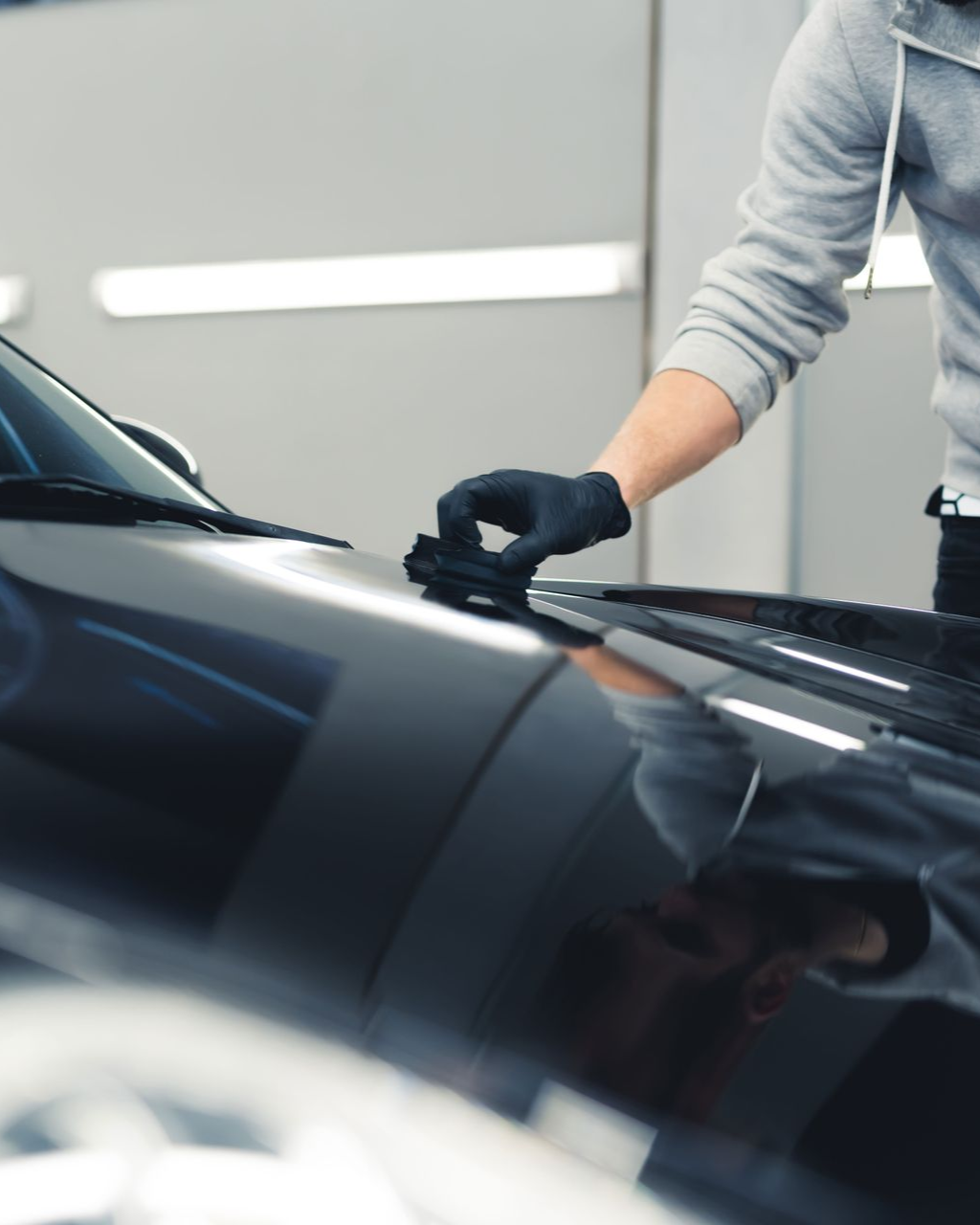 Person in gloves wiping a black car hood with a cloth in a garage