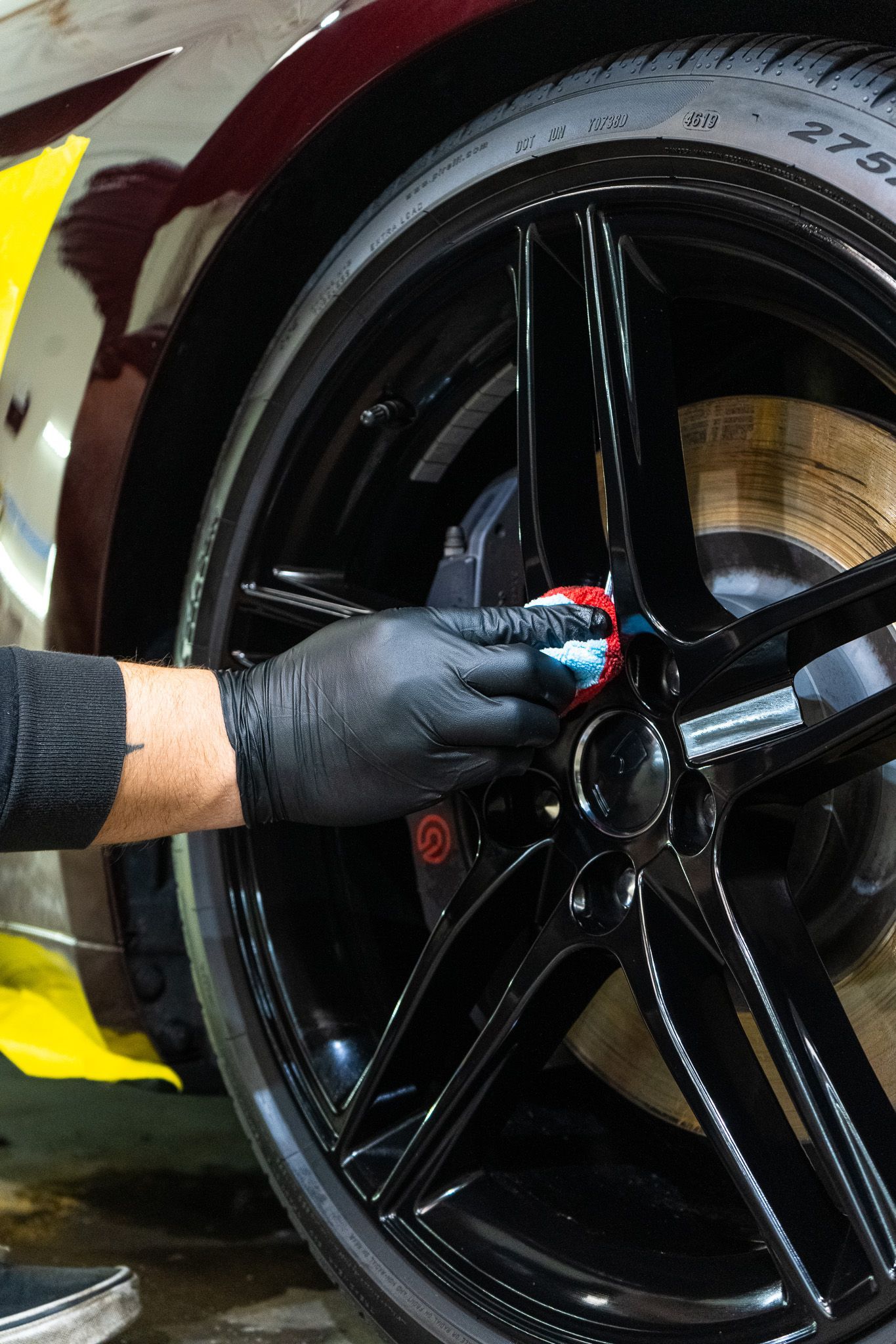 Gloved hand wiping a black car wheel rim with a cloth in a garage