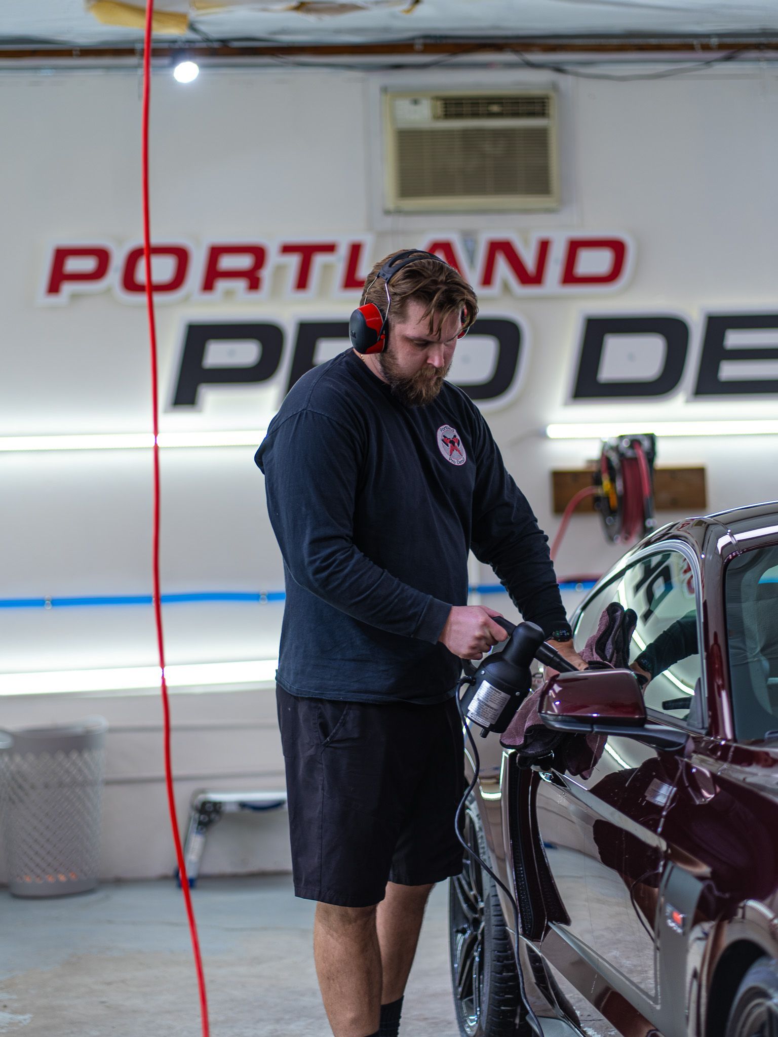 Man in black standing beside a maroon car inside a Portland Pro Detail shop