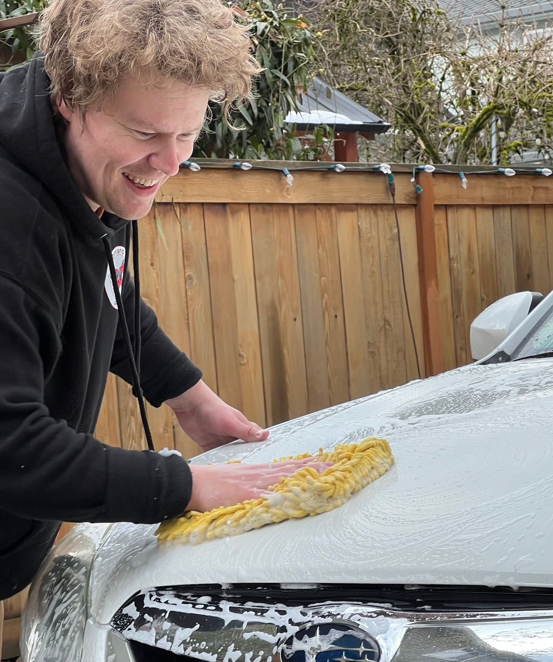Person polishing a beige car with an electric buffer in a garage