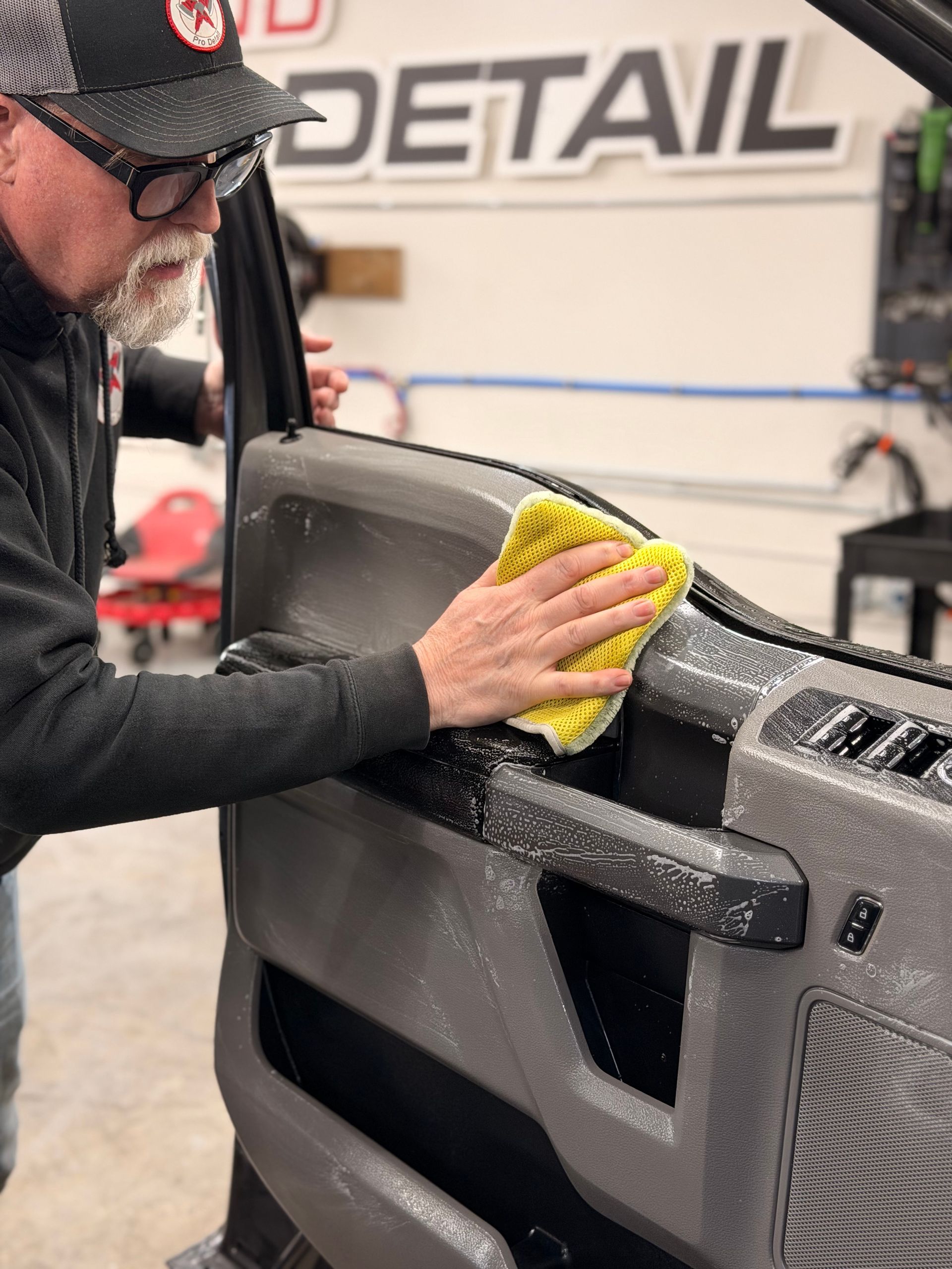 Man cleaning a black vehicle door panel with a yellow cloth at an auto detail shop