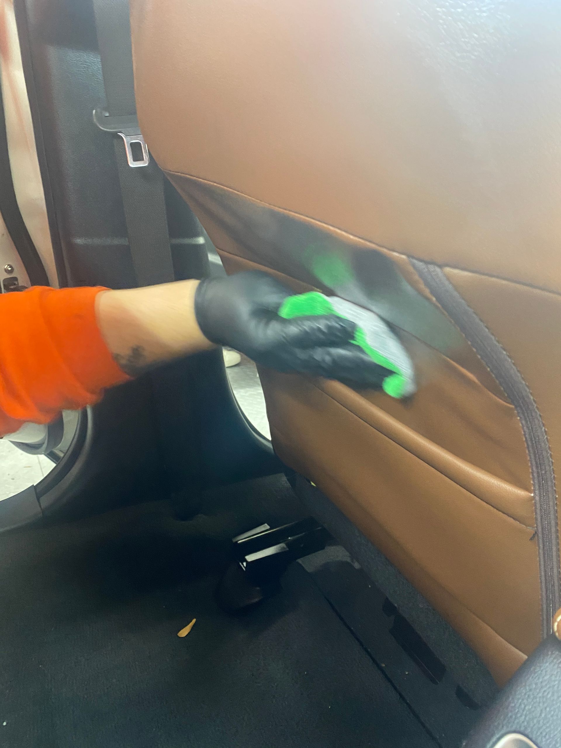 Gloved hand cleaning tan car seat upholstery with a cloth in the back seat