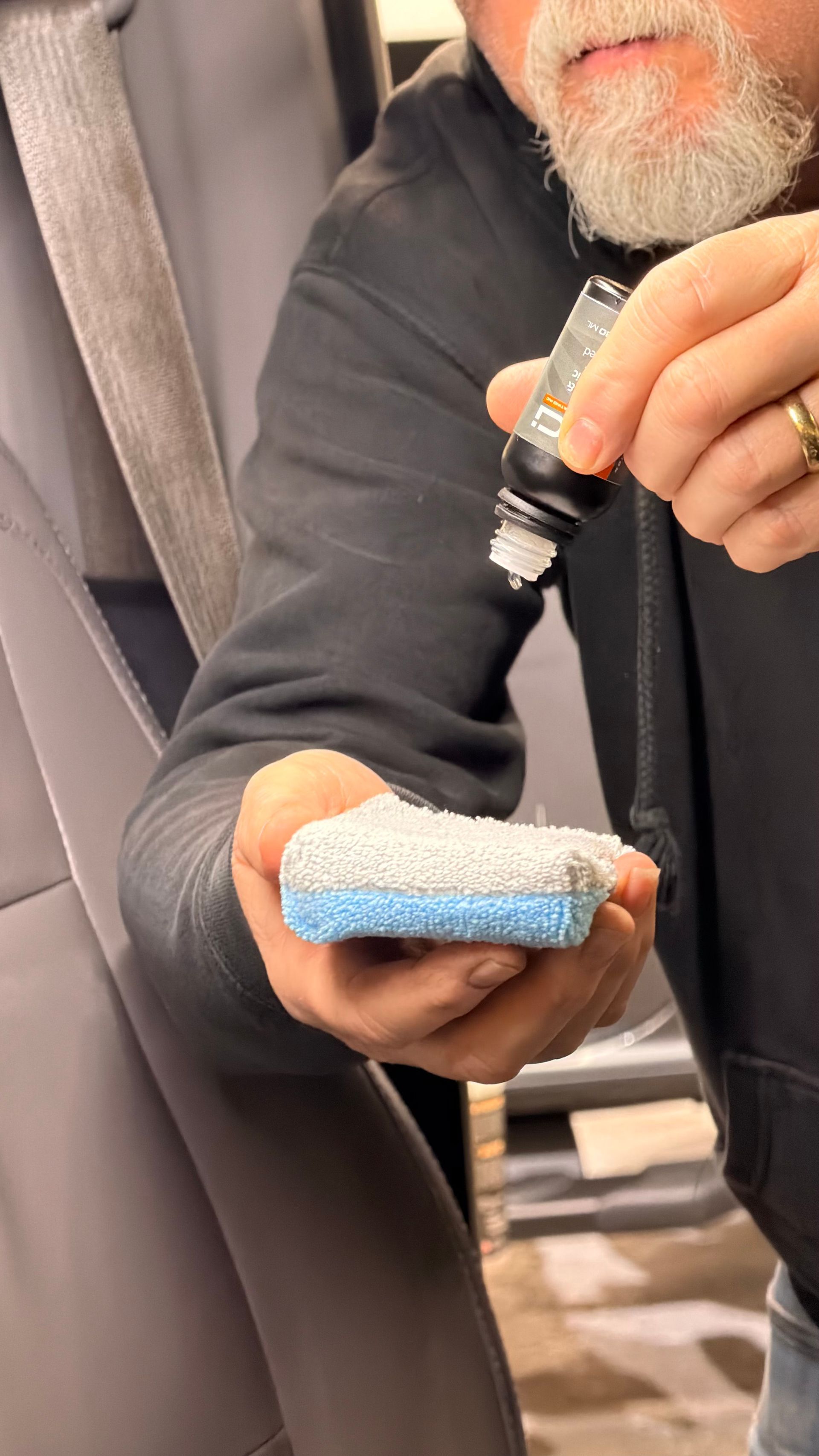 Person holding a small blue foam pad while applying liquid from a bottle in a workshop.