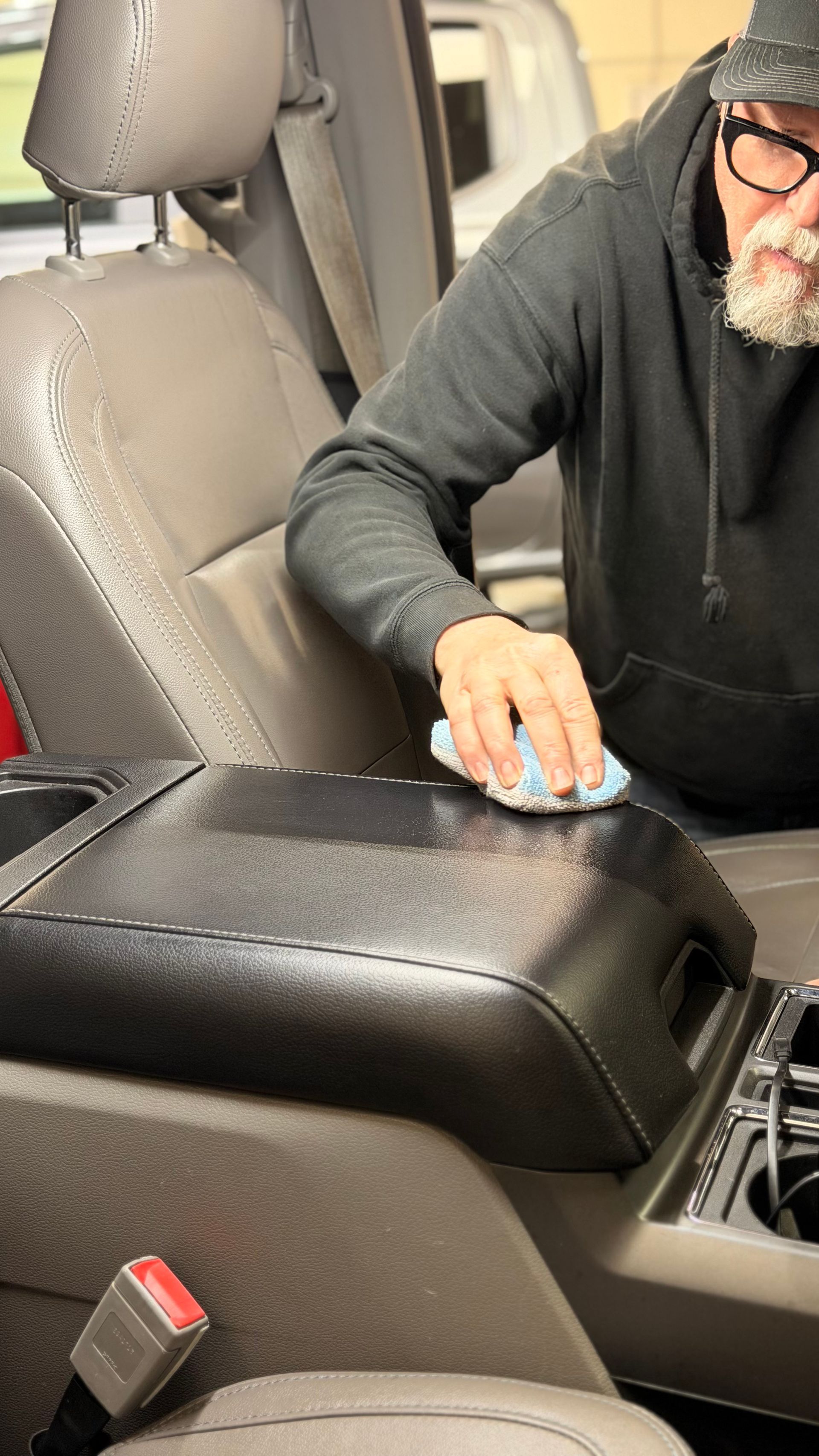 Person cleaning a black leather car armrest with a cloth inside a vehicle