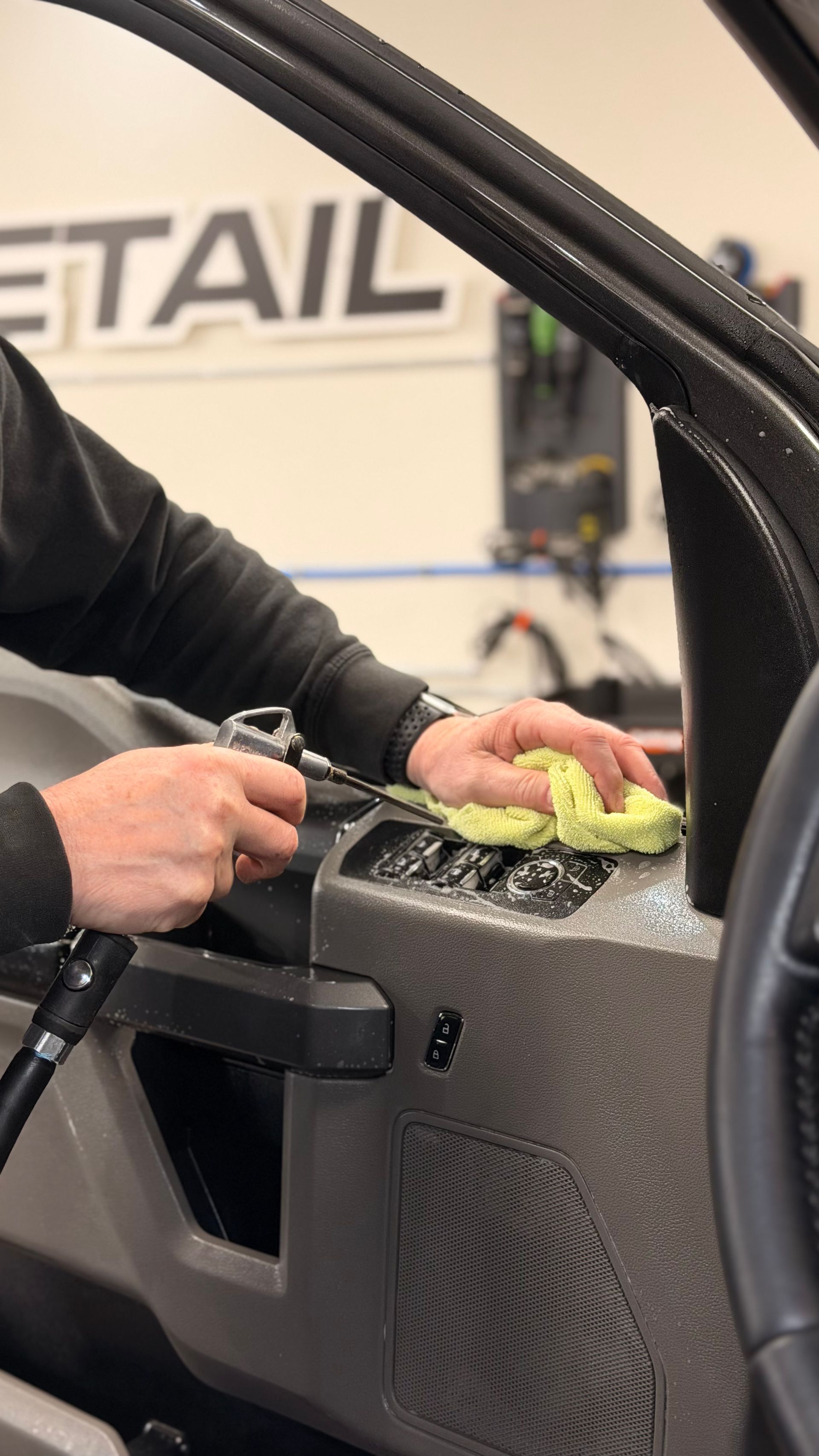 Person cleaning a car door panel with a cloth in an auto detailing shop