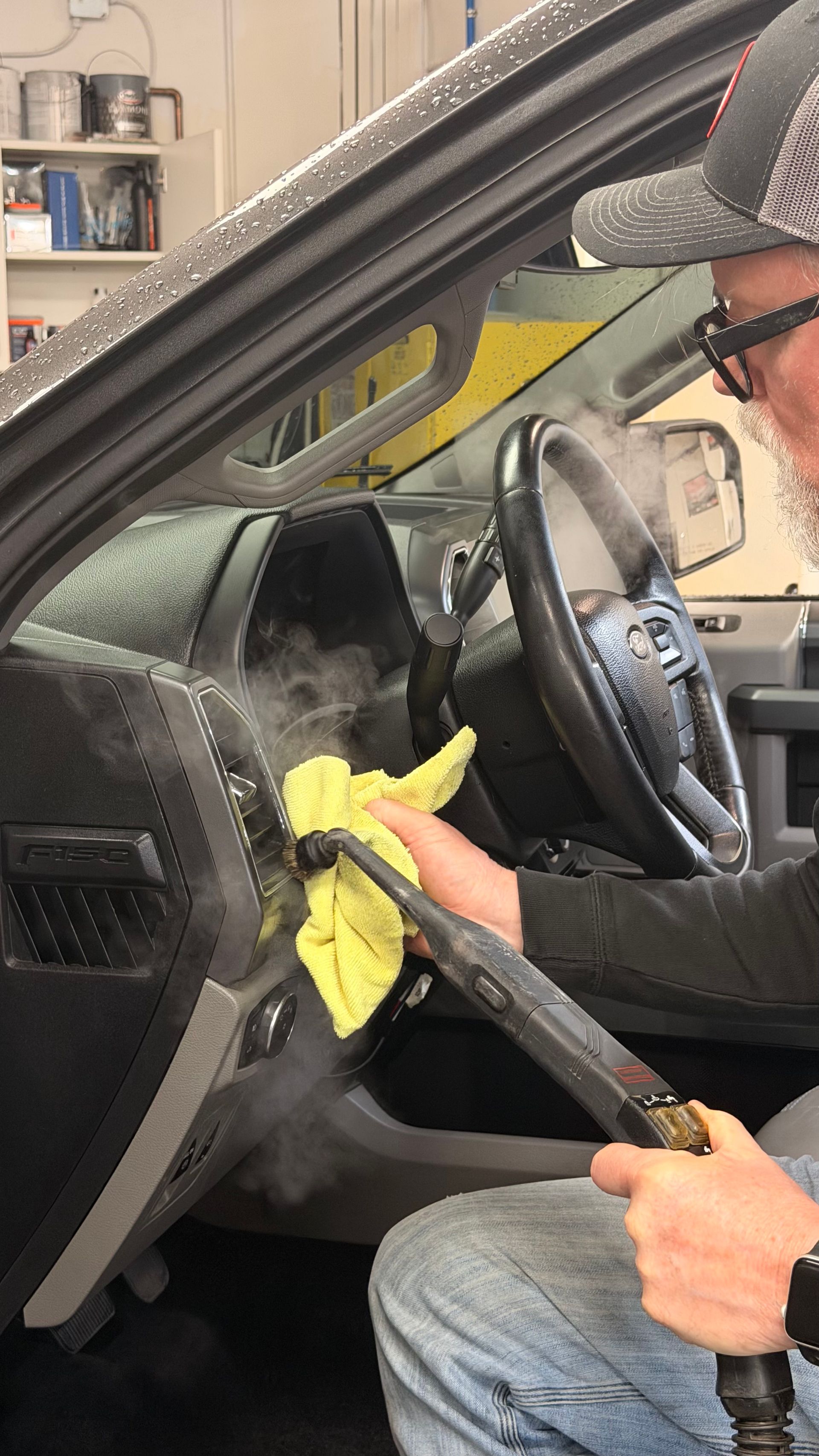Person cleaning a car dashboard with a yellow cloth while seated in the driver’s seat
