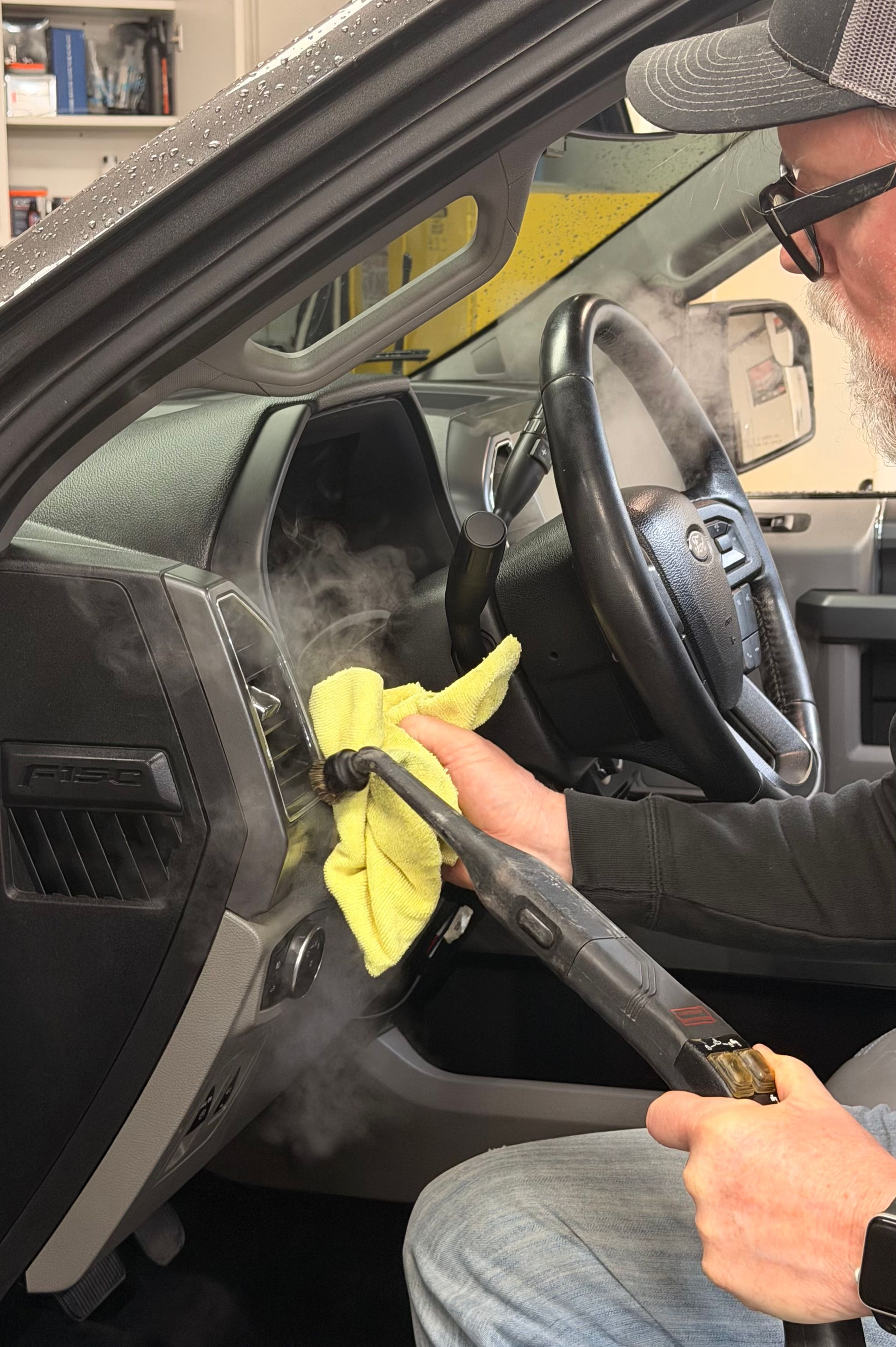 Person wiping a car dashboard with a yellow cloth while seated in the driver’s seat