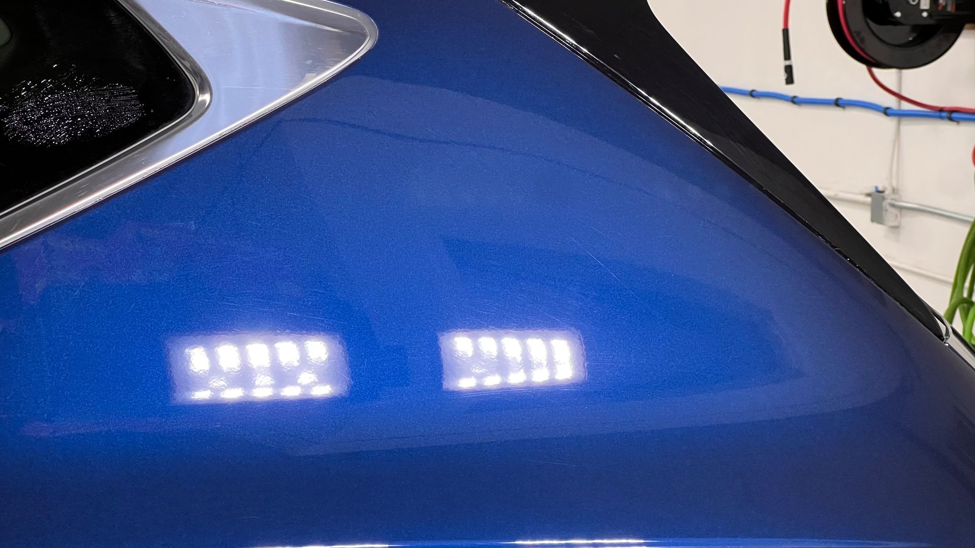 Close-up of a blue car panel with two bright reflections of lights.