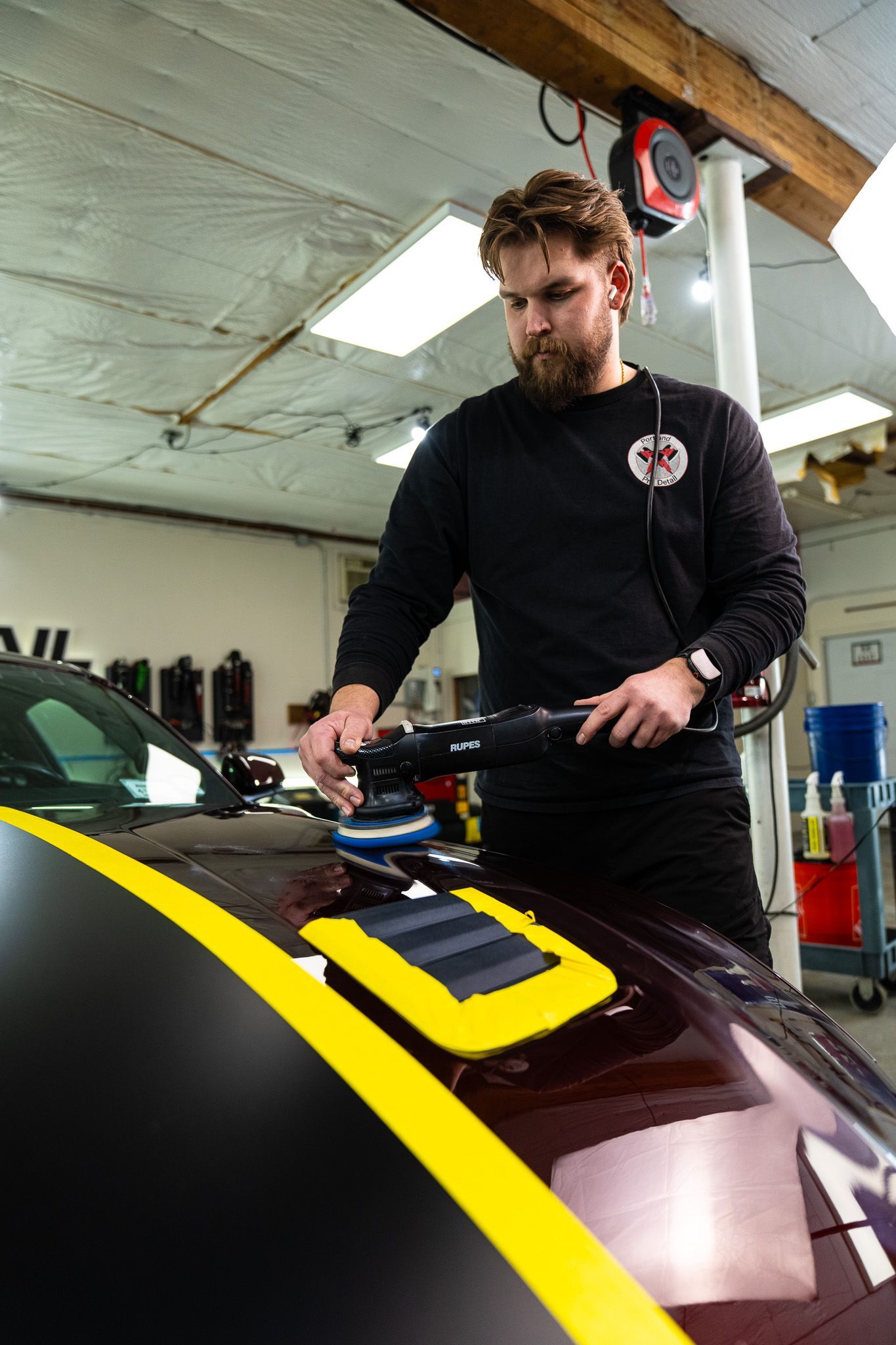 Man polishing the hood of a maroon race car with yellow stripes in a garage