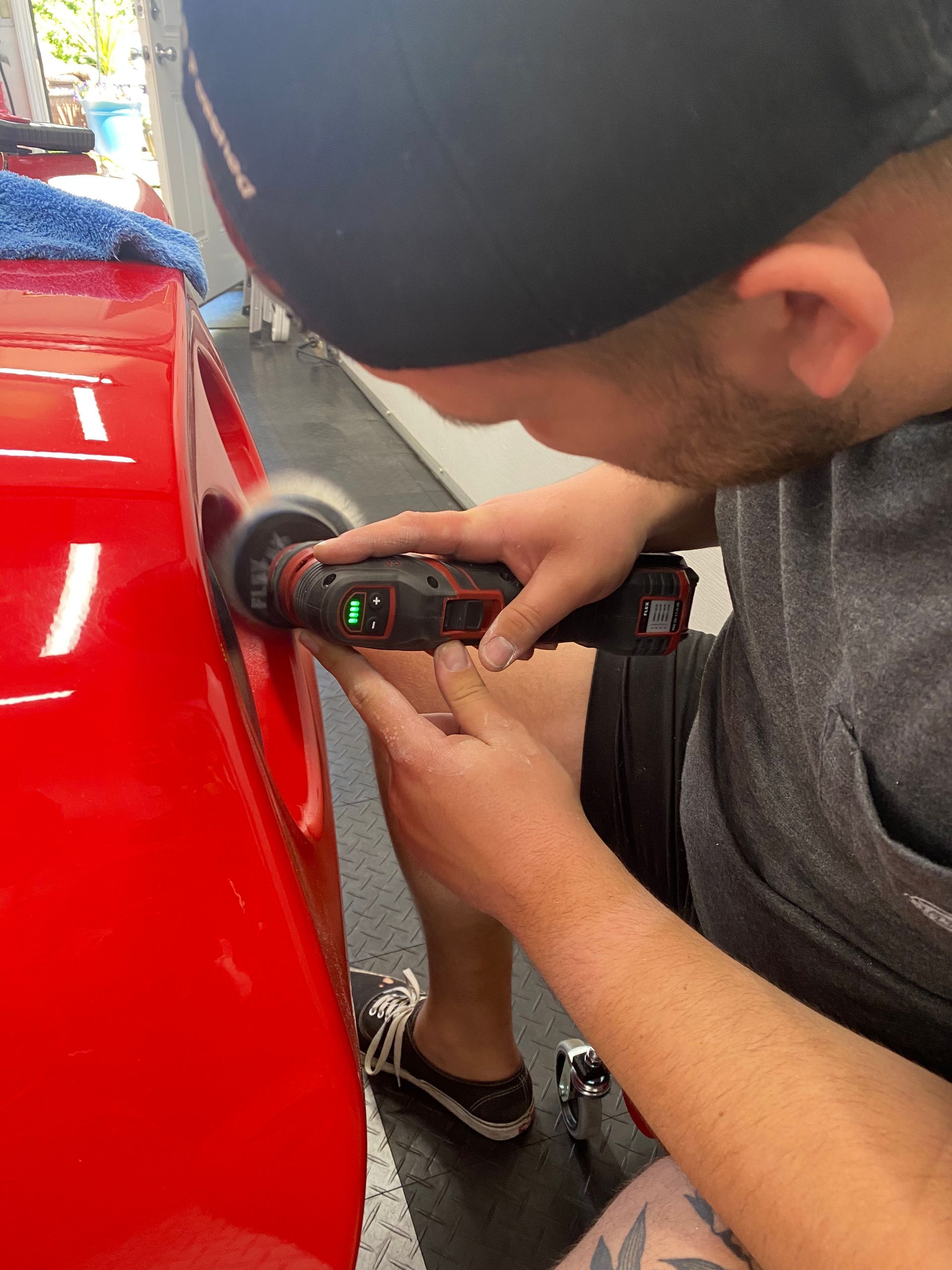 Person using a handheld buffer on a red car panel in a garage