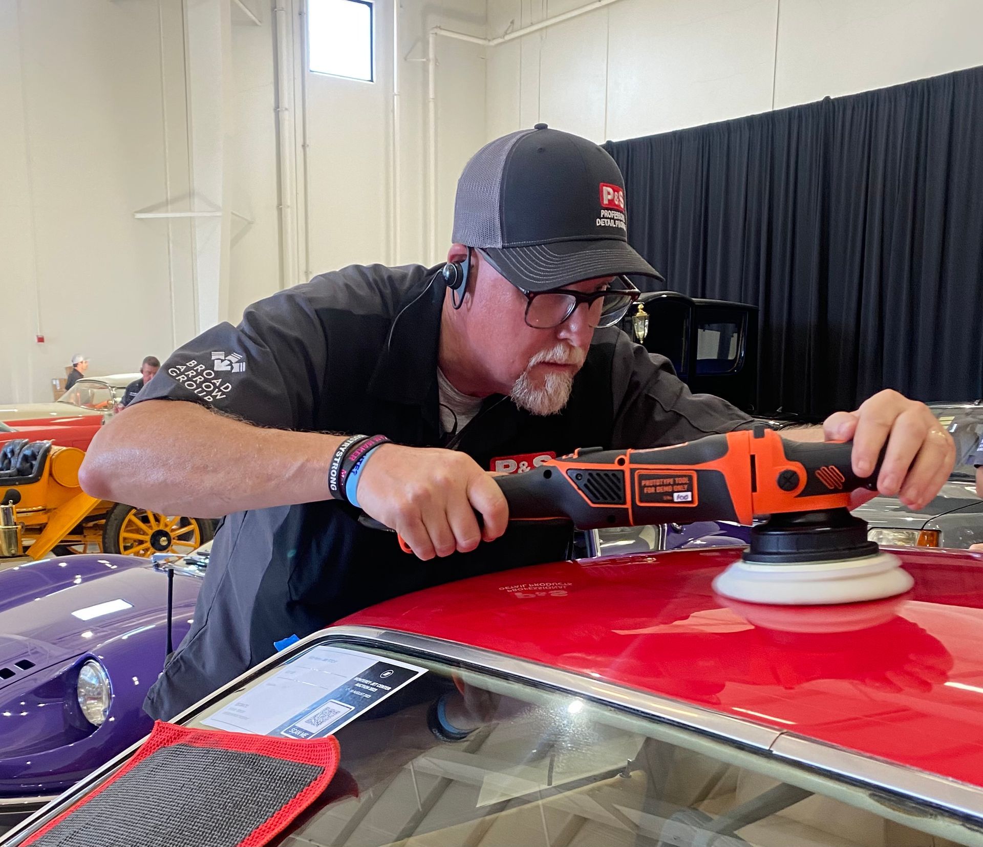 Man polishing a red car roof with an orange buffer in a workshop