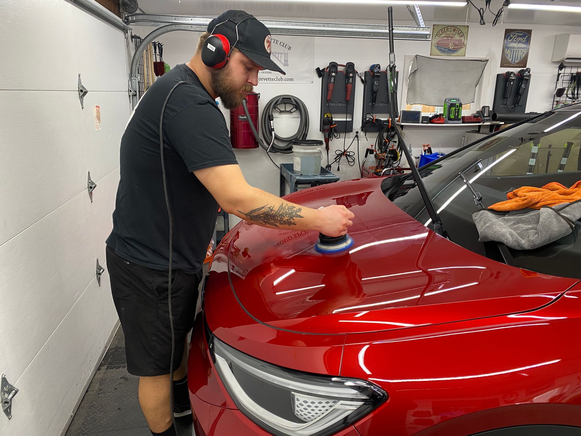 Man polishing a red car’s hood in a garage with a buffing tool