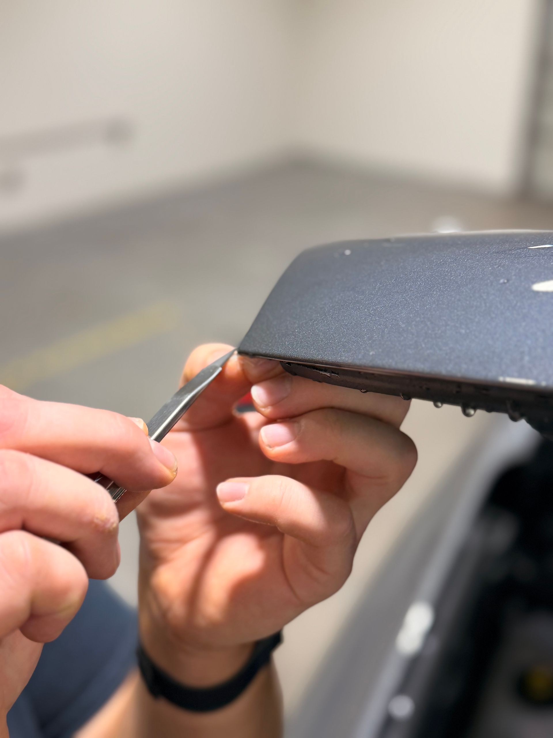 Hands using a small tool to apply a black wrap to a car side mirror cover
