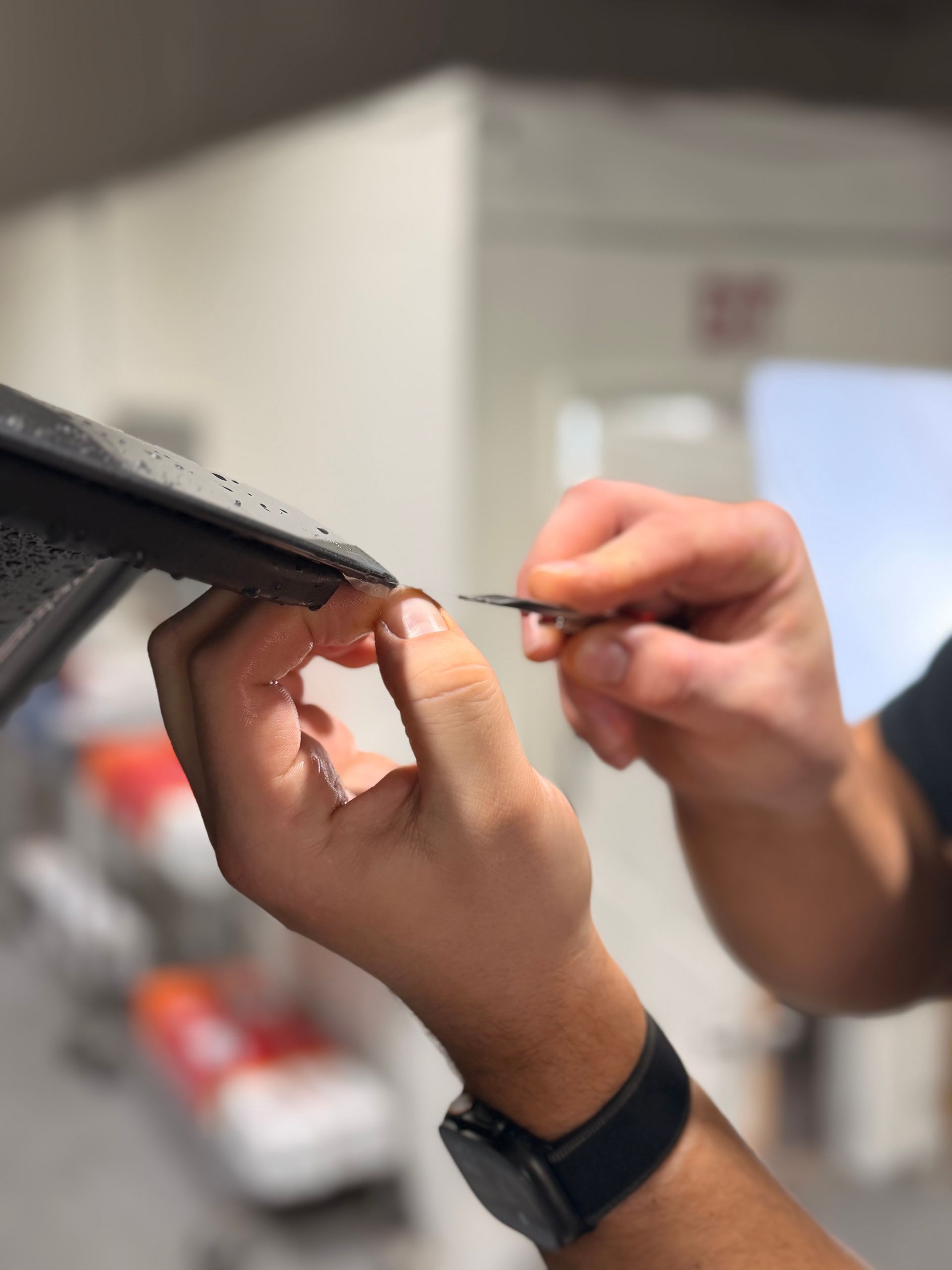 Hands adjusting a black strap or frame with a small tool in a workshop setting
