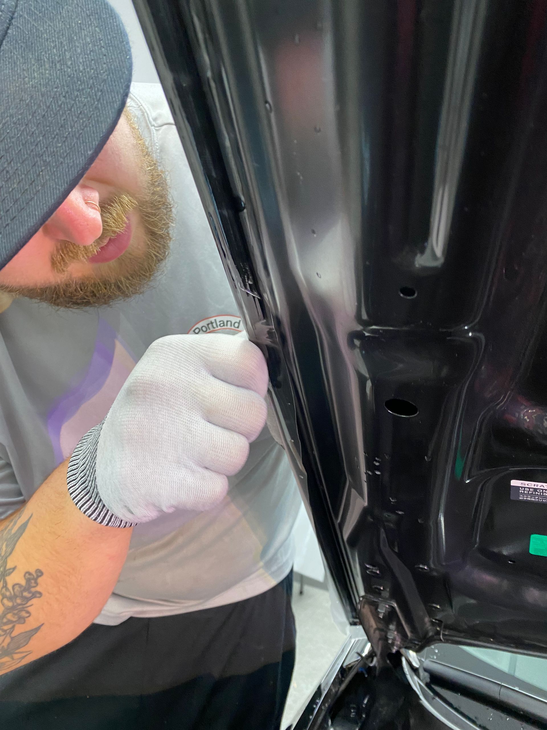 Gloved person inspecting a car door frame with a tool, close-up view inside the vehicle.