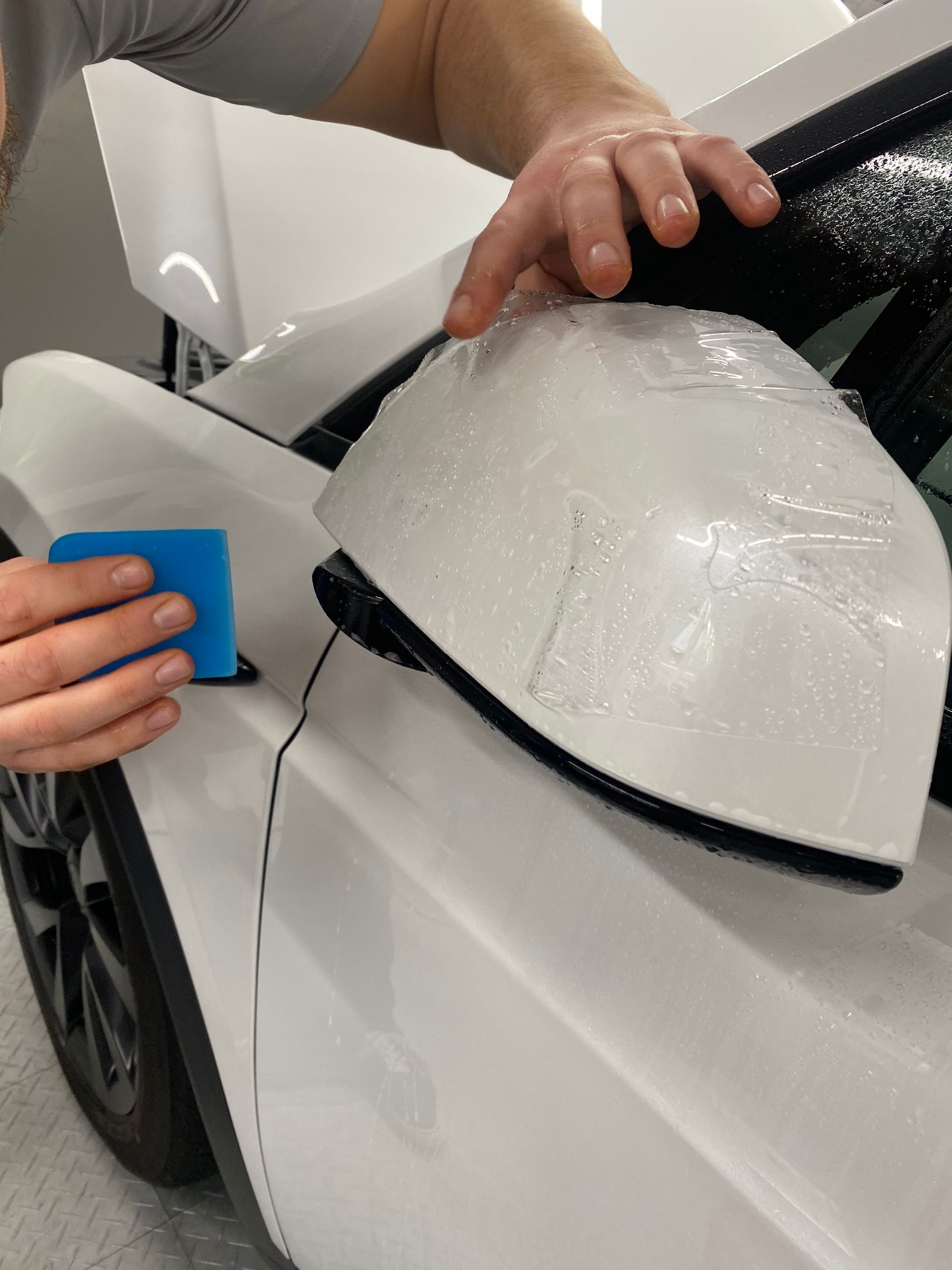 Person applying white wrap film to a car side mirror with a blue squeegee