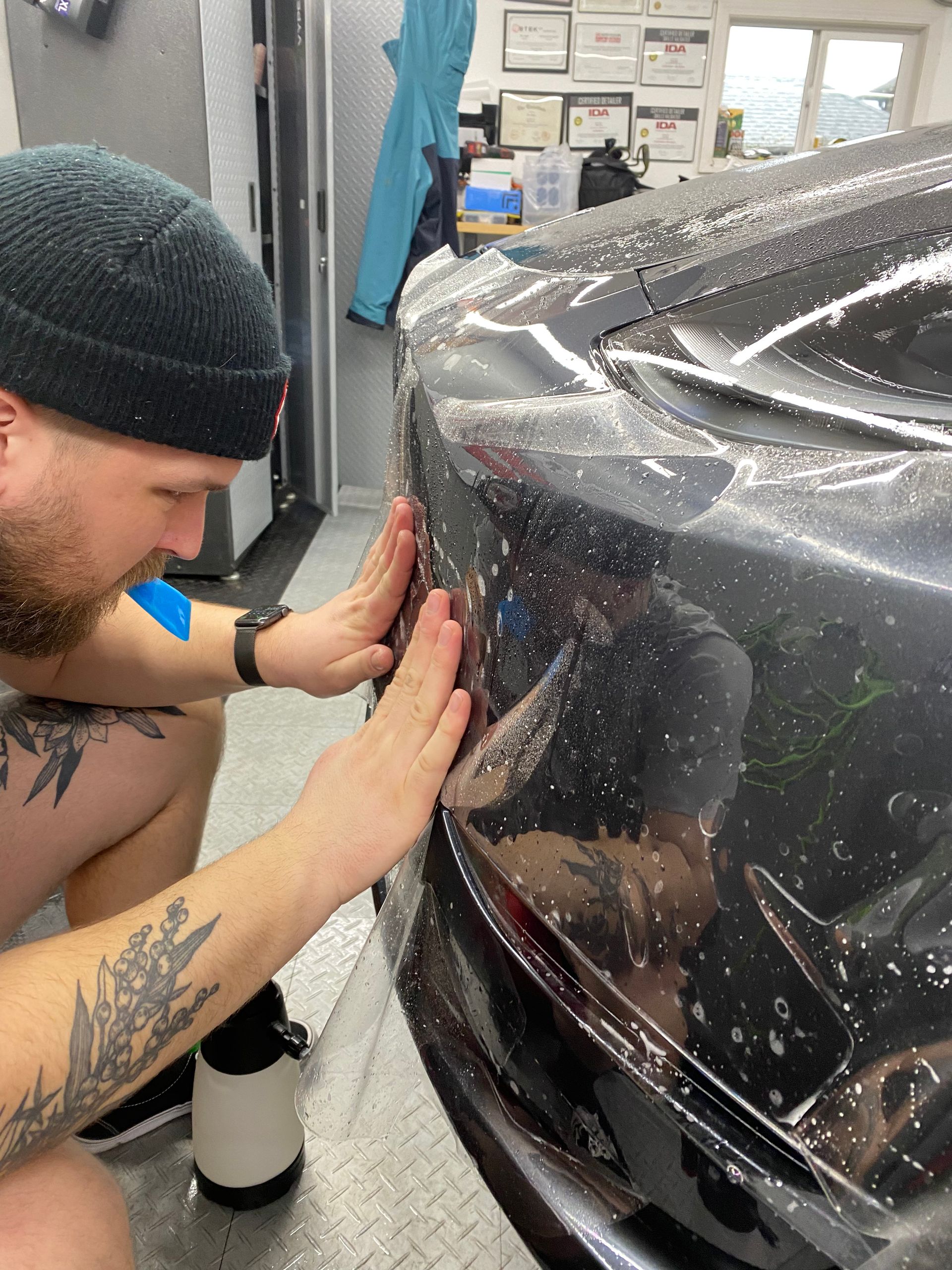 Person applying a clear protective wrap to a car bumper in a workshop