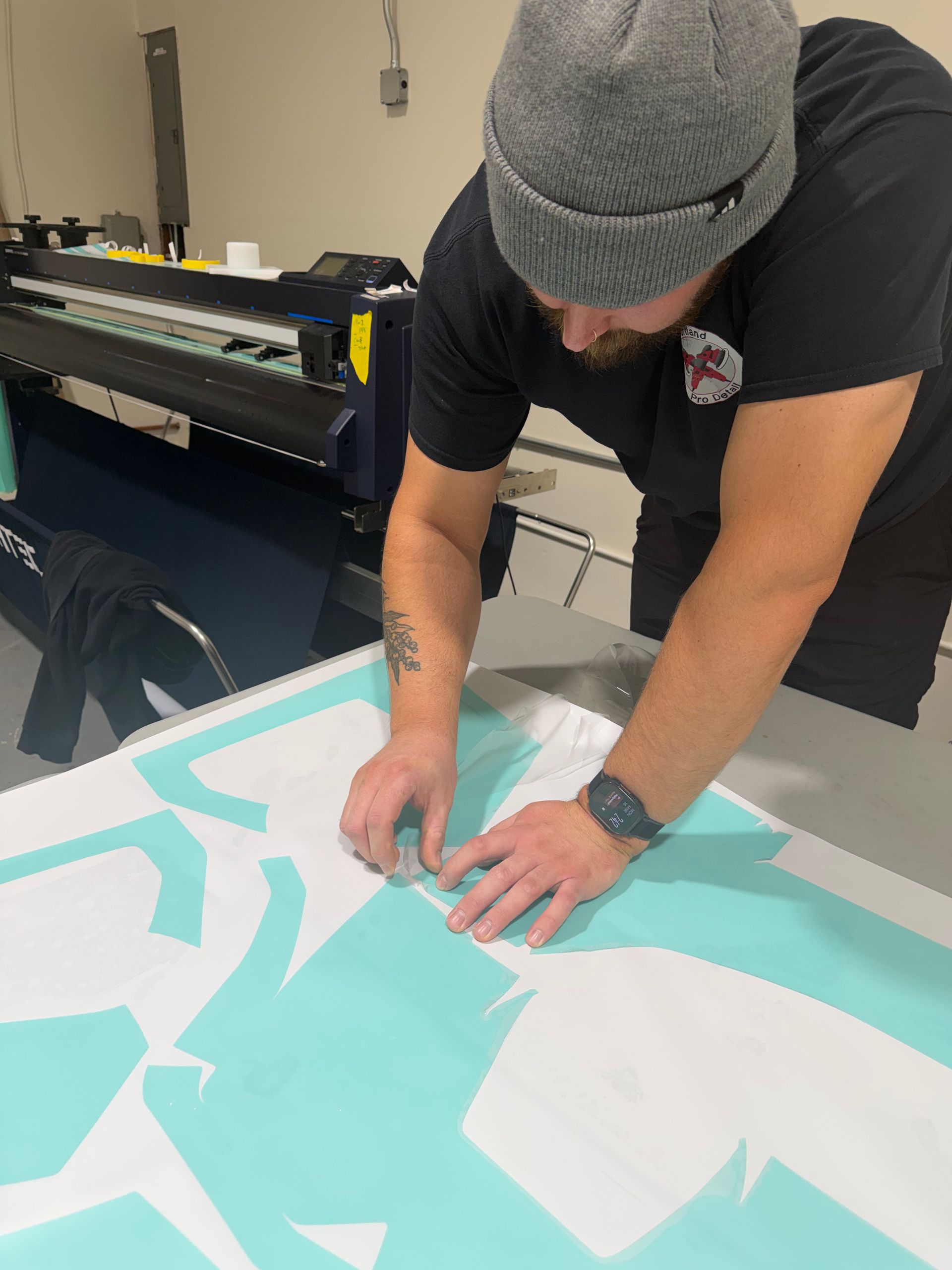Person in a beanie applying a turquoise vinyl decal to a table in a workshop