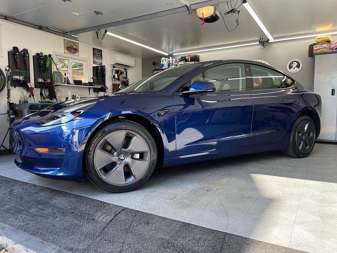 Blue sedan parked in a garage, viewed from the side.