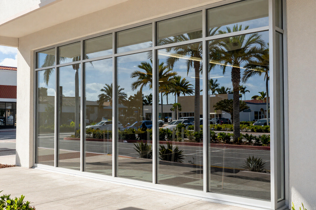 Storefront with large glass windows reflecting palm trees and a sunny parking lot
