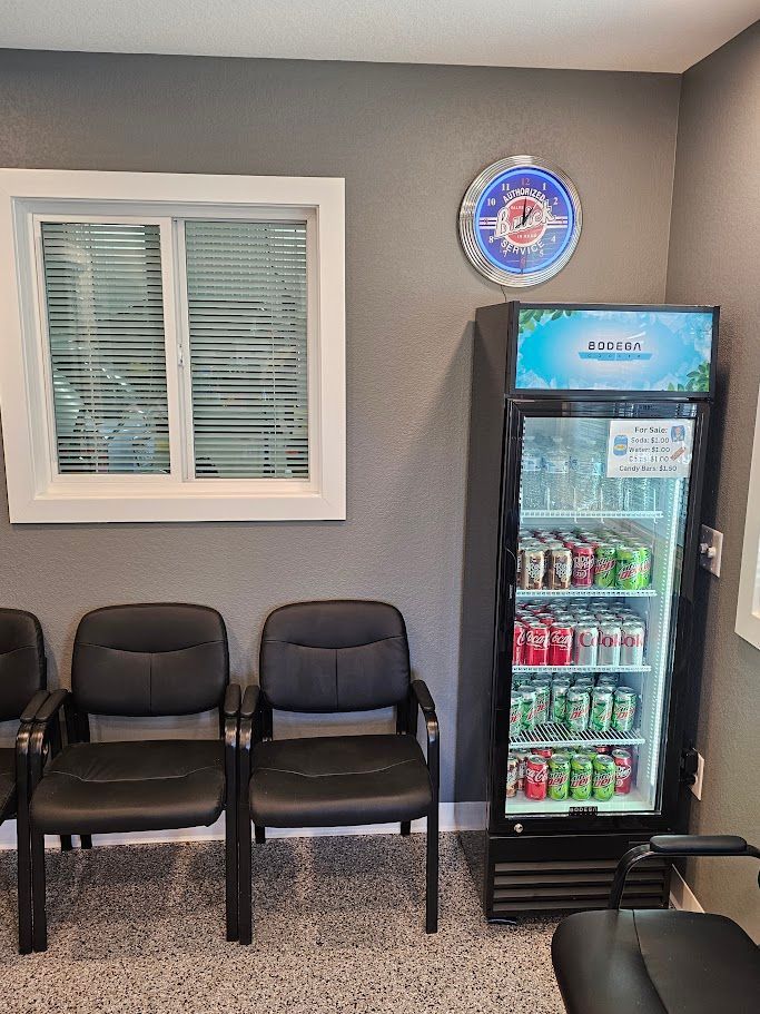 a waiting room with chairs and a refrigerator filled with soda .