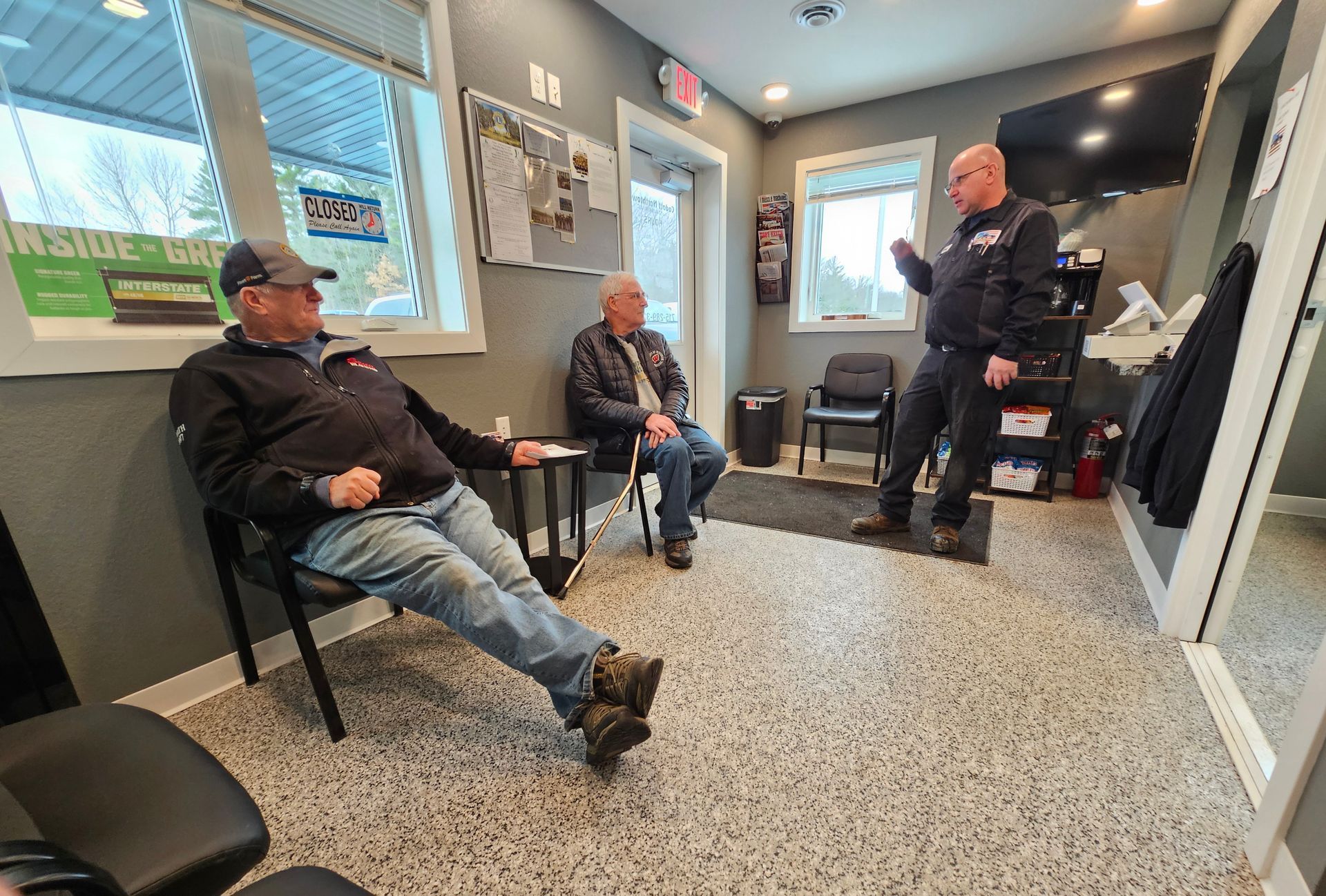 Three men are sitting in a waiting room talking to each other.