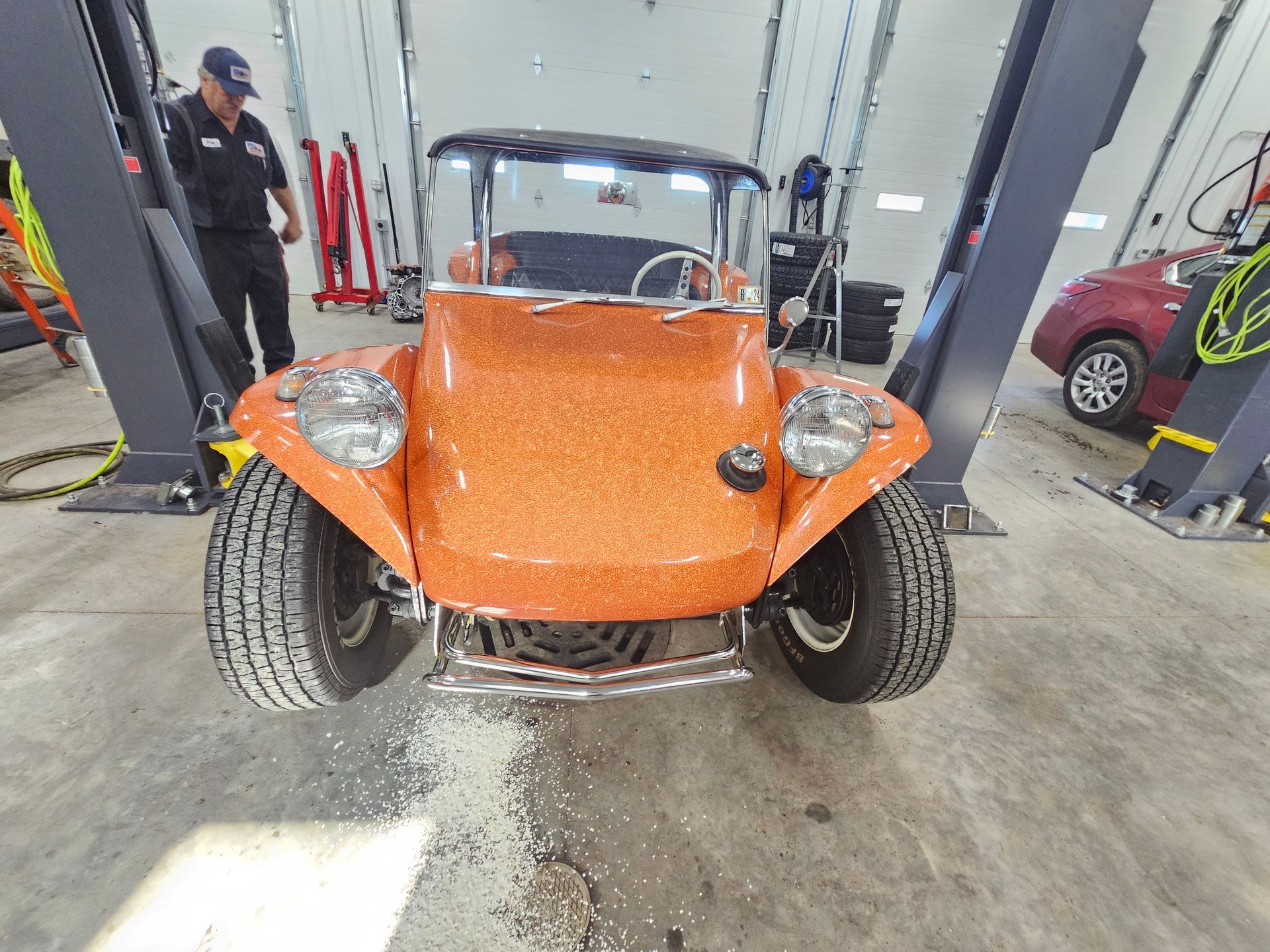 A man is standing next to an orange buggy in a garage.