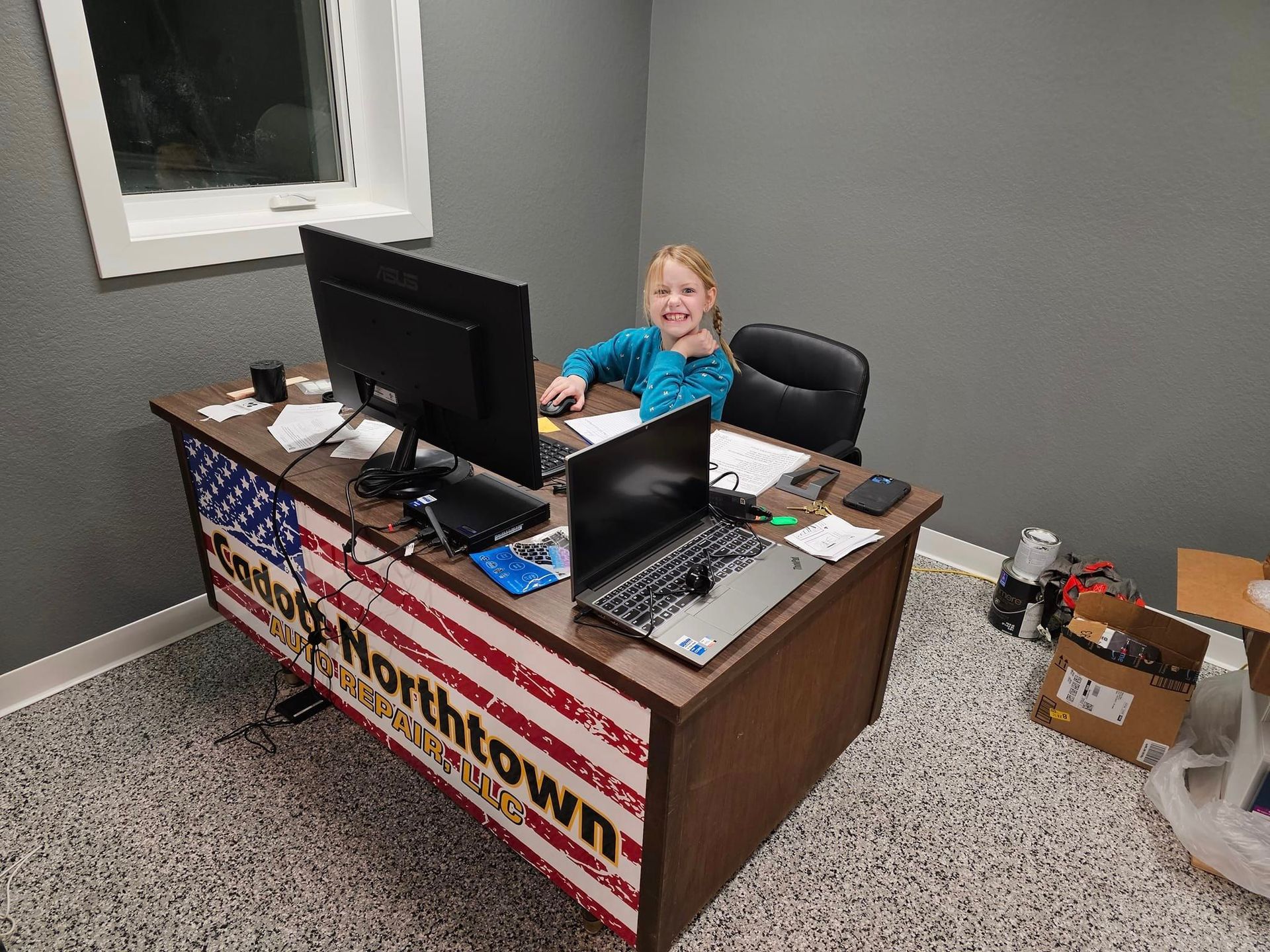 a little girl is sitting at a desk with two computers and a laptop .