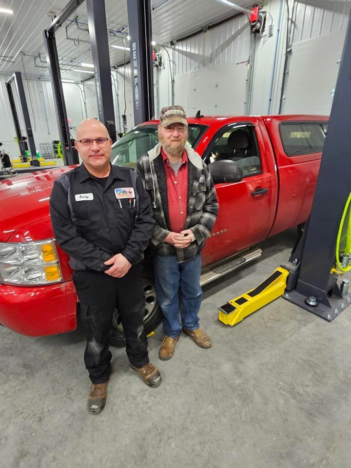 two men are standing next to a red truck in a garage .