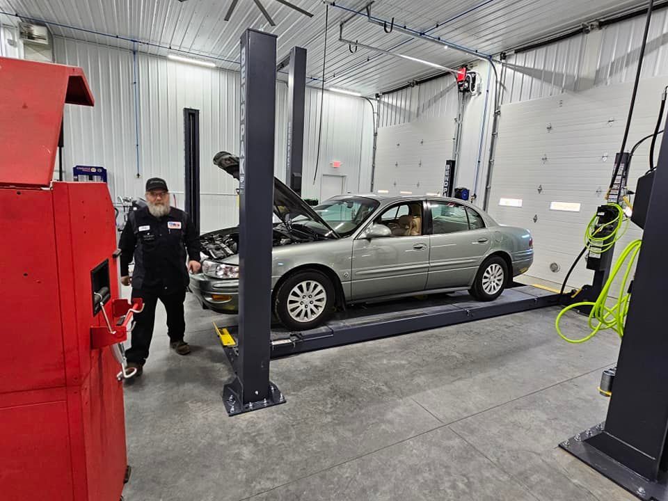 a man is standing next to a car on a lift in a garage .