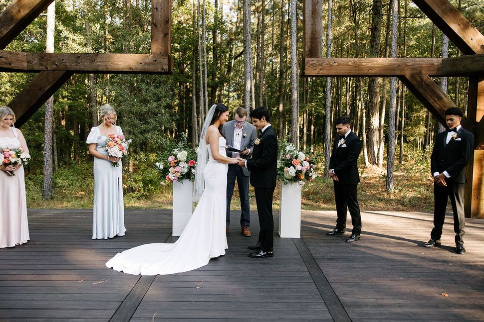 Bride and groom exchanging vows on an outdoor wooden stage during a forest wedding ceremony