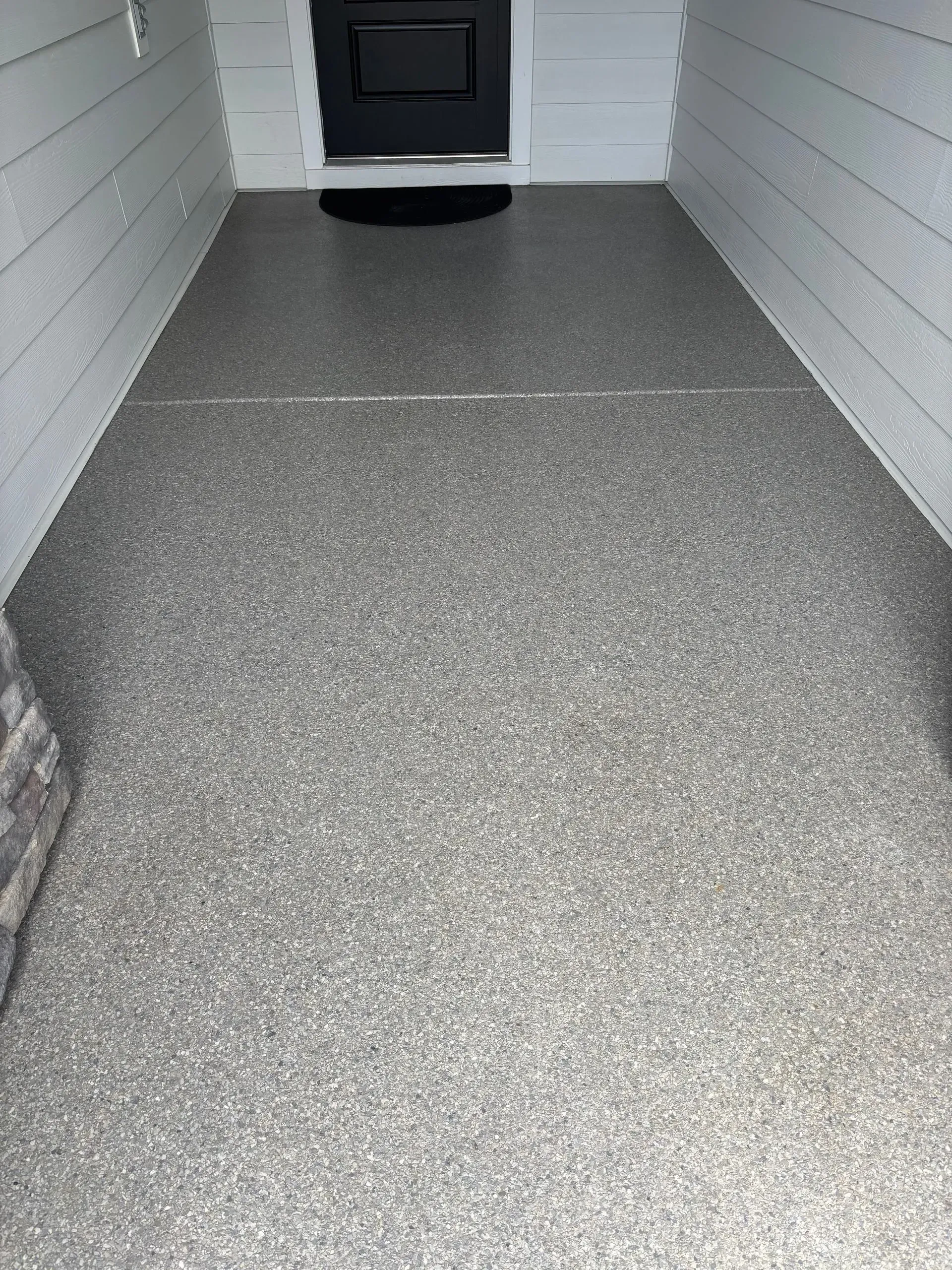 Concrete porch walkway leading to a black front door between white siding walls
