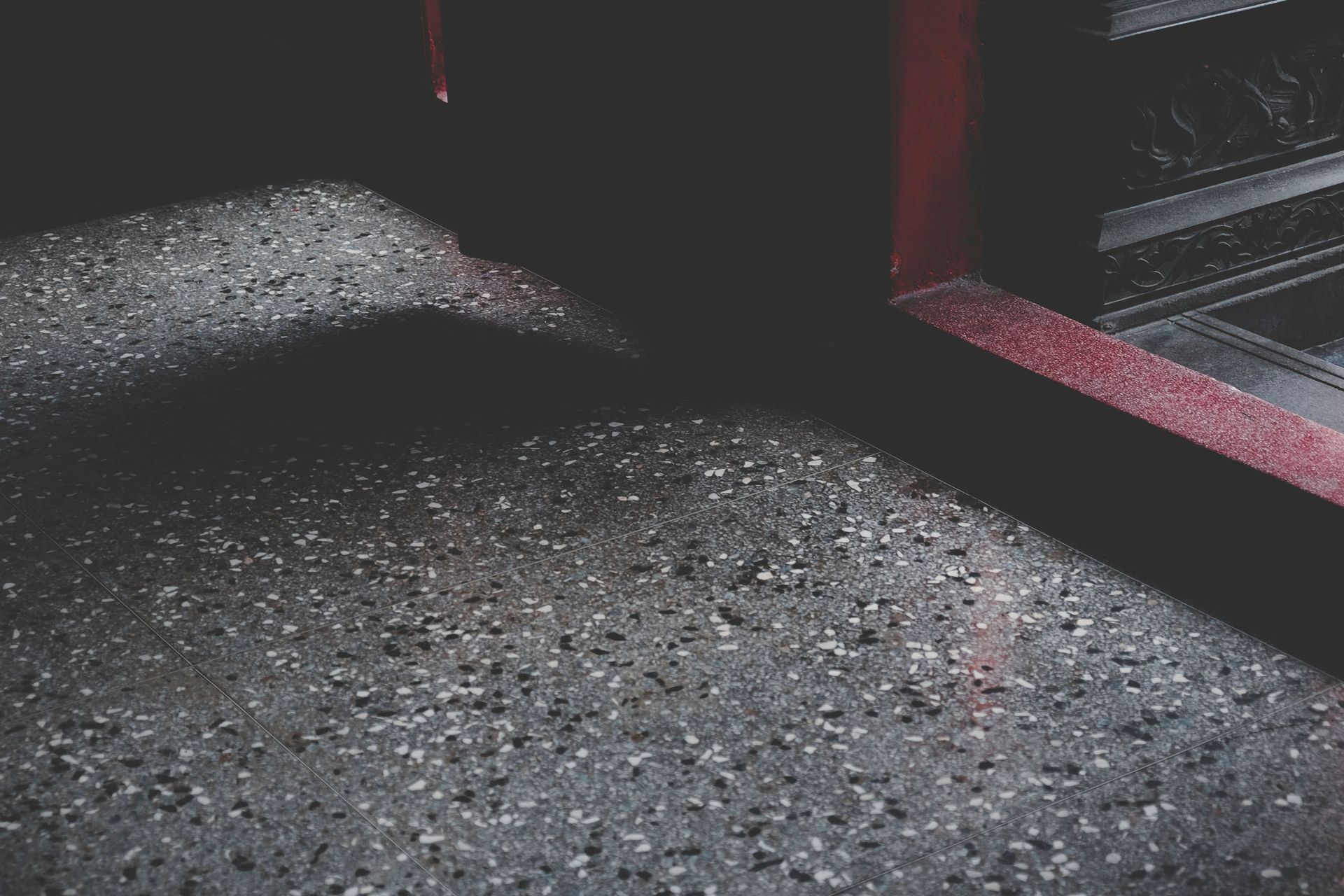 Dim indoor corner with a textured gray floor and red-framed window or wall trim