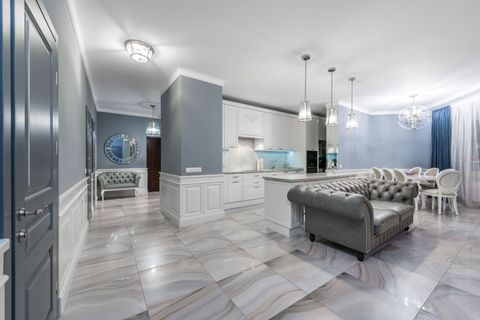 Bright modern open-plan living room and kitchen with gray tufted sofa, marble floors, and white cabinetry