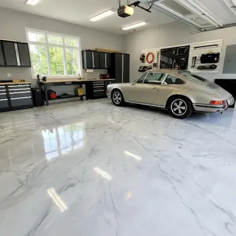 Classic silver sports car parked in a bright, modern garage with glossy white floor and black cabinets