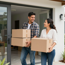 Dos personas sacando cajas de cartón de una casa moderna, sonriéndose mutuamente.