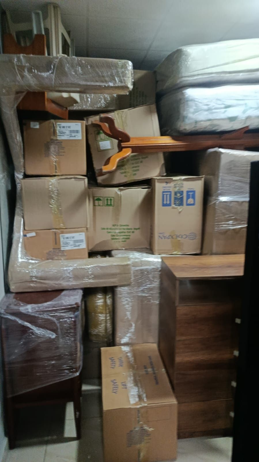 Cajas de cartón apiladas y muebles envueltos, apiñados en un trastero.