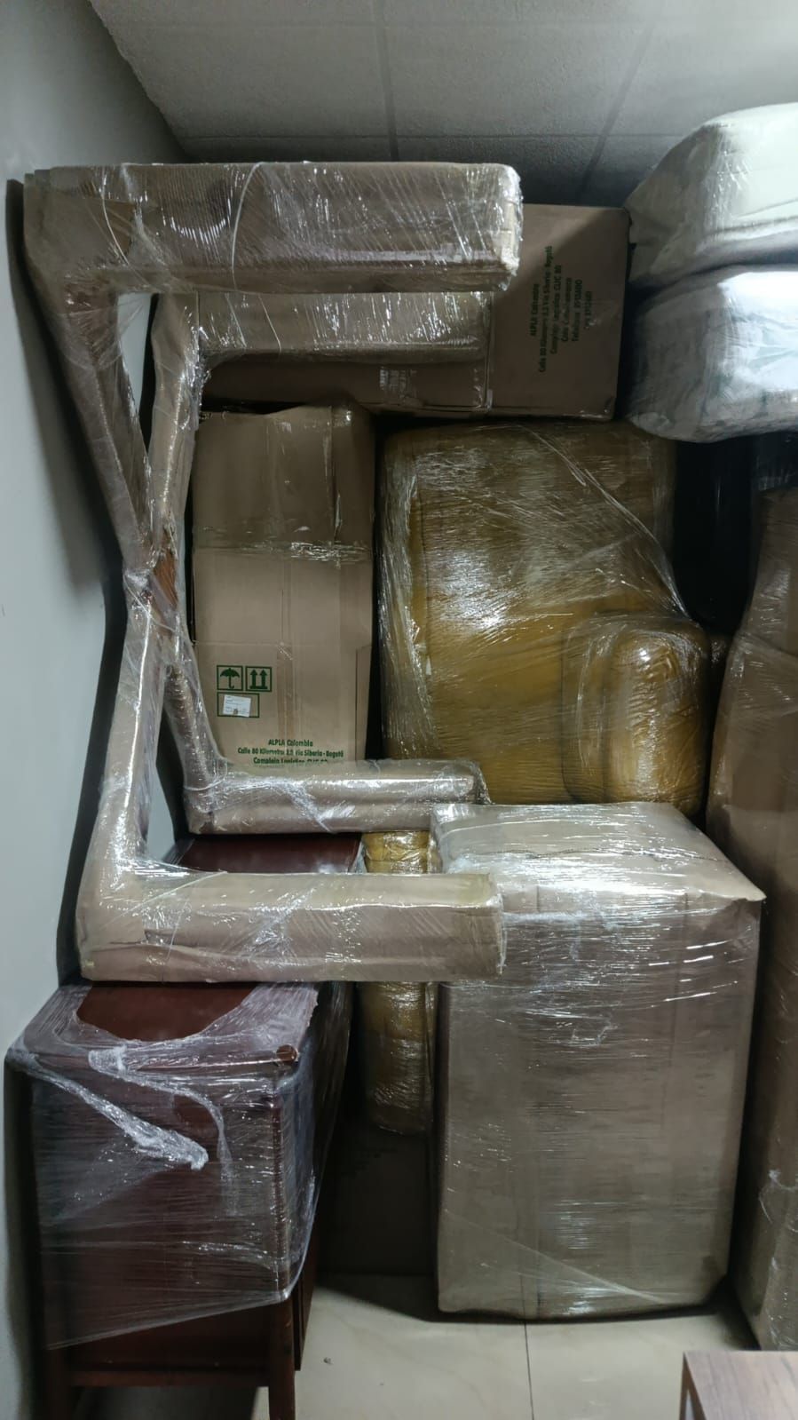 Muebles envueltos apilados y cajas empaquetadas apretadamente en un espacio de almacenamiento.